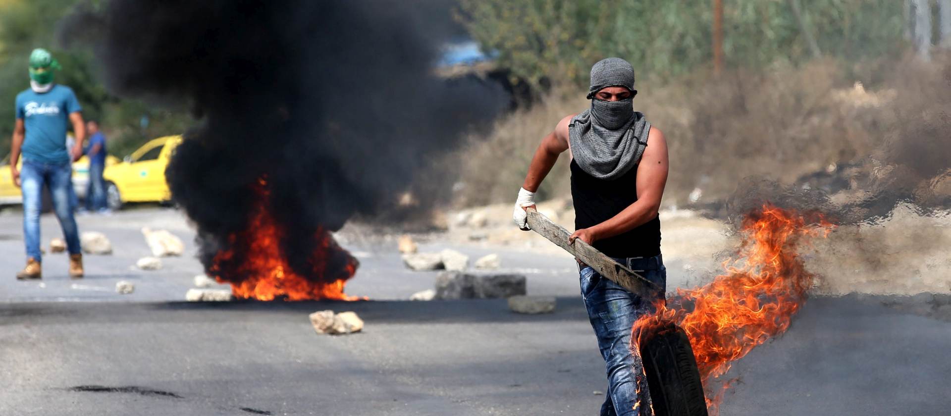epa04985442 A Palestinian protester fuels a burning barricade with a tire during clashes with Israeli security forces in near Al Fawar Refugee camp near Hebron city, 20 October 2015. UN Secretary General Ban Ki-moon will urge calm during a visit on 20 October 2015 to Israel and the West Bank as he seeks to end more than two weeks of the worst street violence in years.  EPA/ABED AL HASHLAMOUN