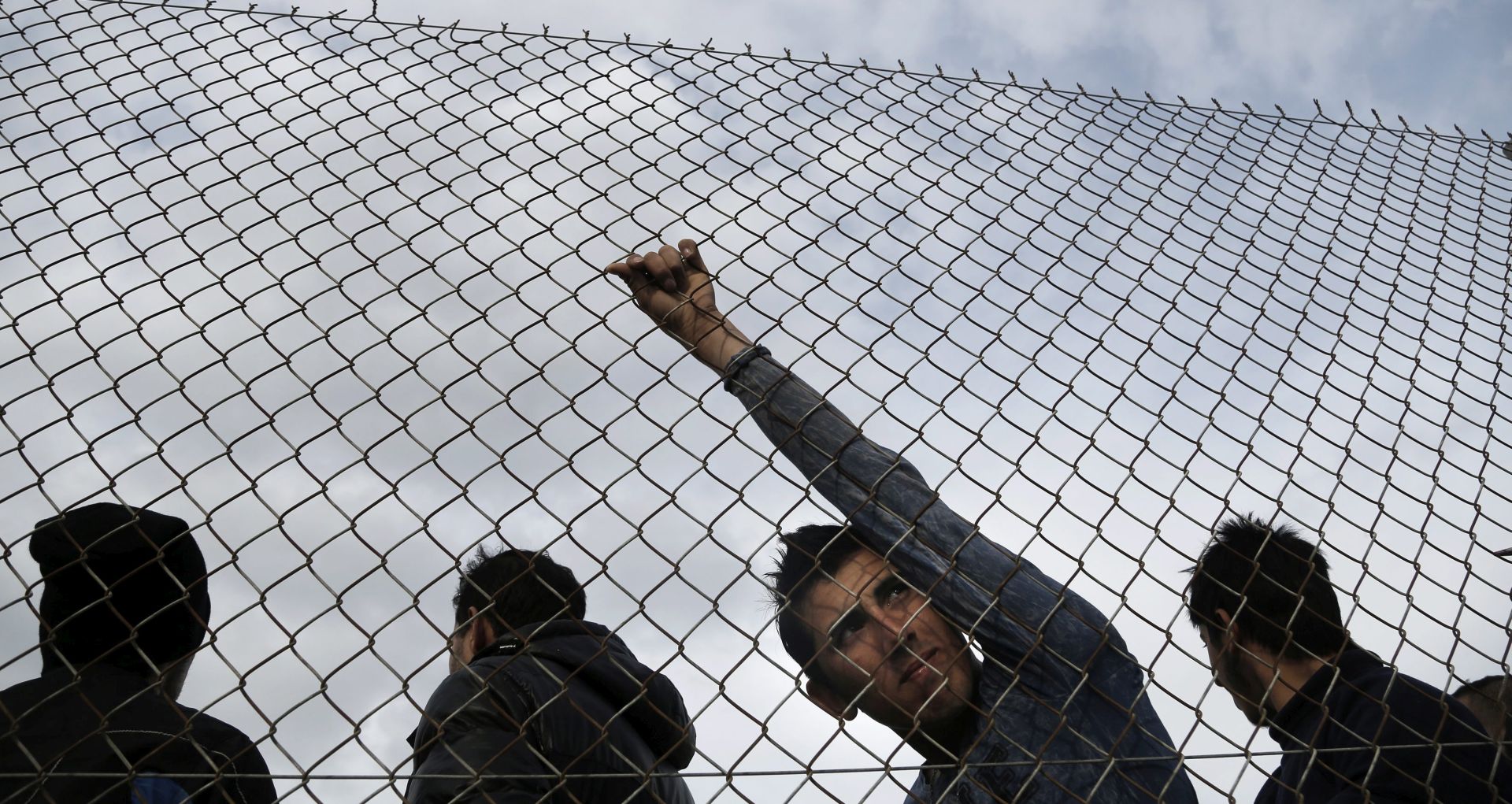 epa05070066 A refugee gazes through the links of a fence while waiting for food to be distributed on the grounds of the former Olympic TAE-KWON-DO Stadium in Athens, Greece, 15 December 2015. The refugees, who are temporarily housed in the stadium, were earlier removed by the Greek Police from Idomeni, north Greece, after being rejected entry to FYROM as economic migrants. Around 800,000 migrants and refugees are estimated to have arrived in Greece since the beginning of the year, with most moving on - sometimes unhindered - to wealthy northern European countries.  EPA/YANNIS KOLESIDIS