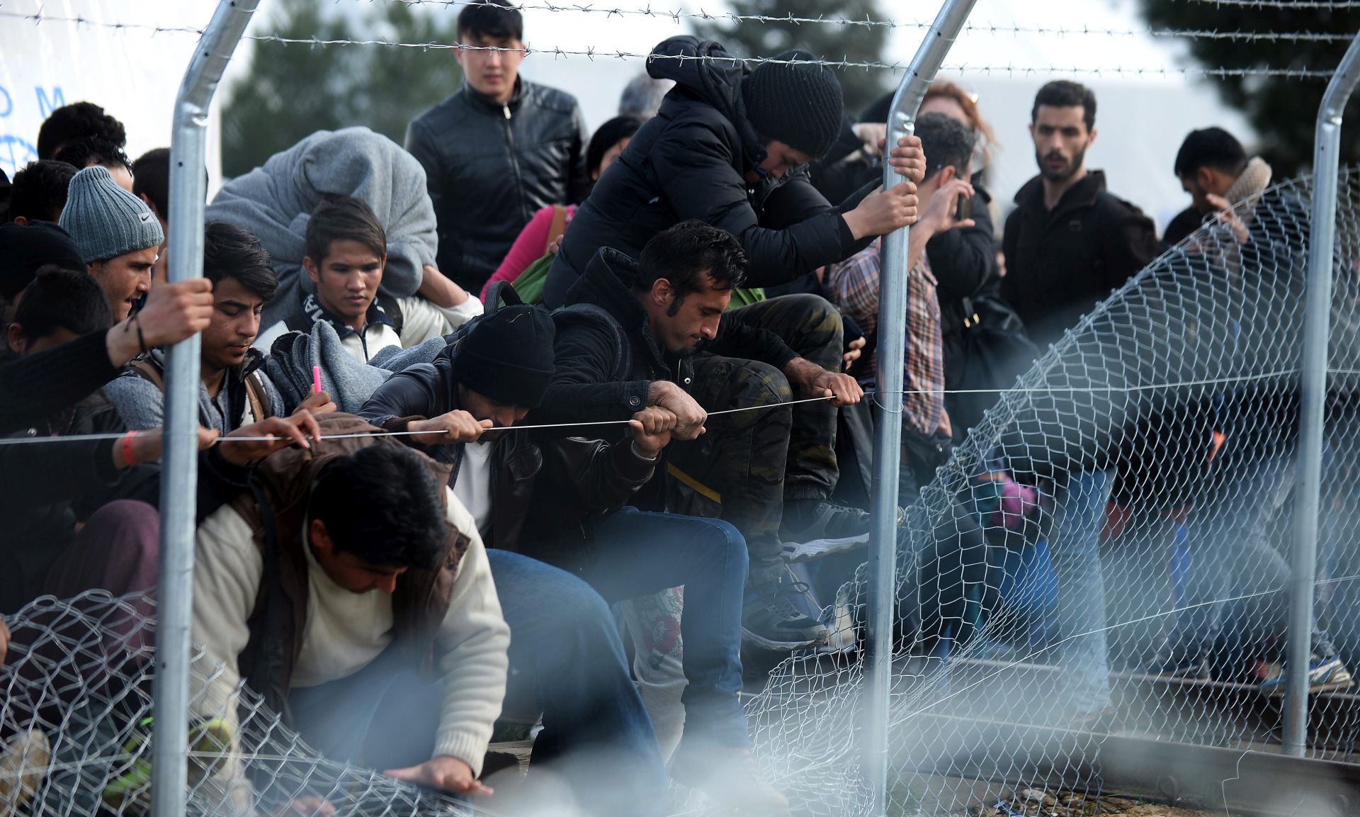 epa05175489 Migrants try to cross through a fence at the Greek-Macedonian border, near the Macedonian city of Gevgelija, 22 February 2016. Macedonia confirmed that it is only allowing Syrian and Iraqi refugees through, matching a decision by its northern neighbour, Serbia. Around 5,000 people were waiting at the border on 22 February, local reports said, quoting witnesses. All want to continue their journey across Macedonia, Serbia, Croatia, Slovenia and then Austria, with Germany the final goal for most.  EPA/NAKE BATEV