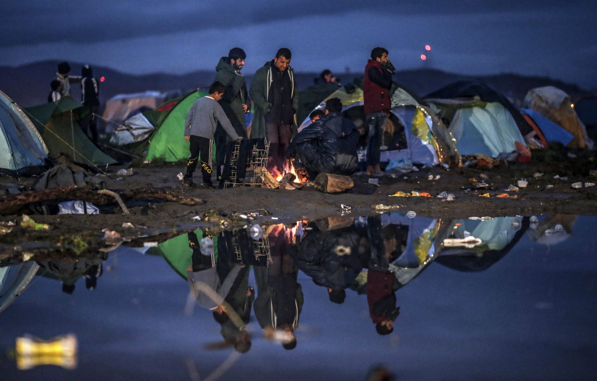 epa05204975 Refugees stand between tents in a camp at the border between Greece and the Former Yugoslav Republic of Macedonia (FYROM), near Idomeni, northern Greece, 10 March 2016. After Slovenia, Croatia, Serbia and Macedonia have sealed their borders to the migration flow, tens of thousands of people are left stranded in Greece, where most migrants enter the European Union to continue on to countries in Europe. Greece estimates that more than 25,000 migrants are presently on its territory, with more than half stuck at the makeshift camp Idomeni, on the border with Macedonia.  EPA/VALDRIN XHEMAJ