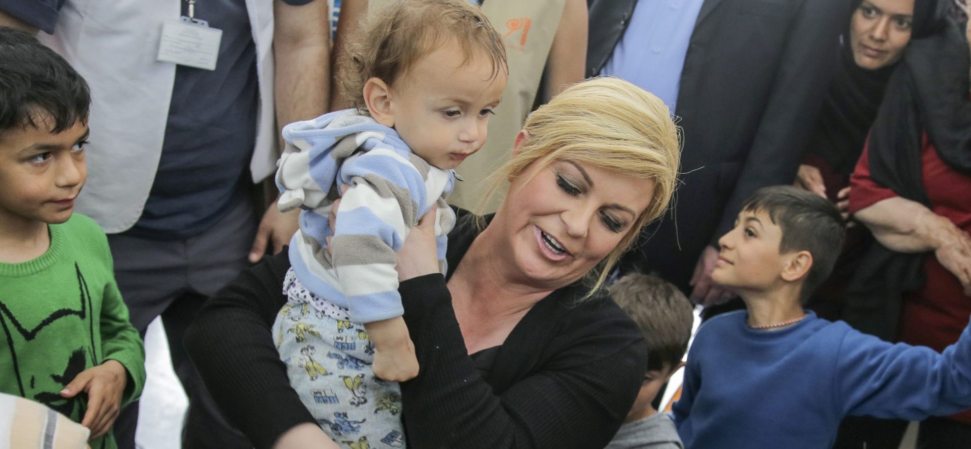 epa05256611 Croatian President Kolinda Grabar-Kitarovic (C) holds a child and talks with refugees stuck in the registration and transit camp for refugees near Gevgelia, Former Yugoslav Republic of Macedonia (FYROM), on 13 April 2016. The Macedonian, Slovenian and Croatian Presidents are on a two days work visit to Macedonia to gather first hand information about the refugee situation at the border to Greece.  EPA/VALDRIN XHEMAJ