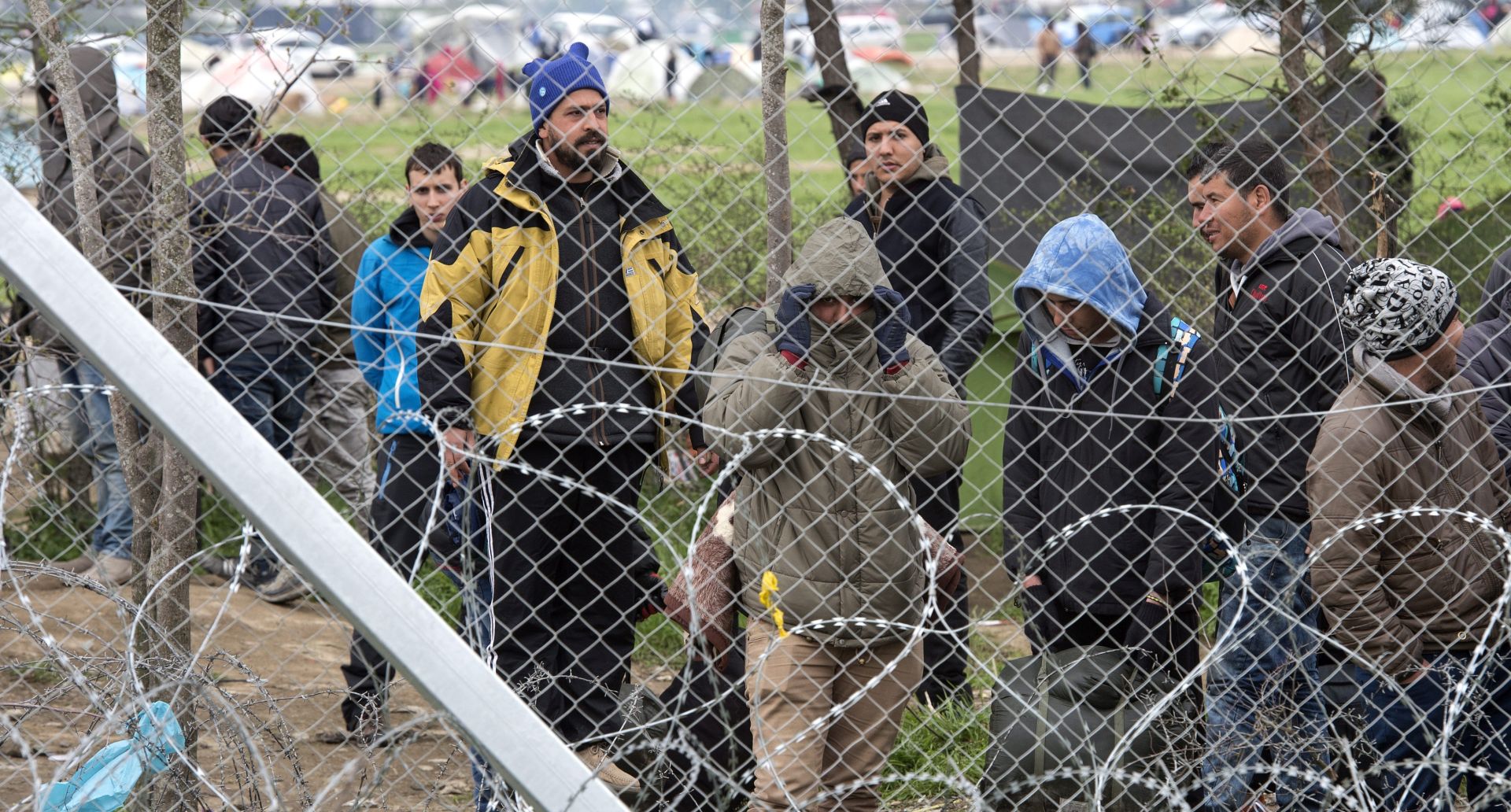 epa05232515 Refugees stand behind the fence, on the Greek side of the border near Gevgelia, The Former Yugoslav Republic of Macedonia, 27 March 2016. More than 10,000 refugees and migrants are still waiting at the makeshift camp near Idomeni to enter Macedonia and continue onto EU countries.  EPA/GEORGI LICOVSKI