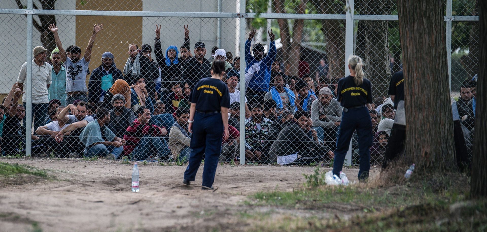 epa05341011 Migrants chant the slogan 'Freedom' as they protest demanding better conditions and faster administrative process deciding about their asylum claim as armed security guards and a Hungarian police officer look on at a closed reception center near the Serbian border in Kiskunhalas, Hungary, 01 June 2016. According to reports, the migrant processing center houses migrants that are to be deported from Hungary.  EPA/SANDOR UJVARI HUNGARY OUT