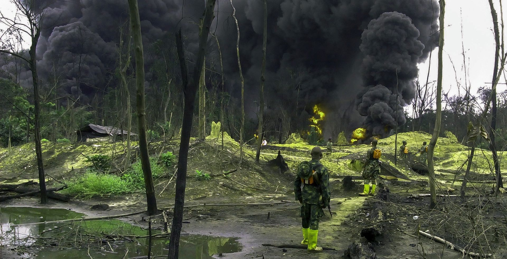epa04805450 Nigerian soldiers of the Joint Task Force look on during the destruction of an illegal oil refinery in Oteghele Forest, Warri South-West Local Government Area of the Niger Delta, Southern Nigeria, 17 June 2015. According to Nigerian authorities, approximately 150,000 barrels of oil are stolen per day directly from the thousands of kilometres of pipelines across the oil rich delta states. It is estimated that 25 percent of this illegal oil tapped from the pipelines is then taken to illegal and makeshift oil refineries hidden in forests and amongst the mangroves of the Niger Delta. Nigeria is the largest crude oil producer in Africa.  EPA/STR