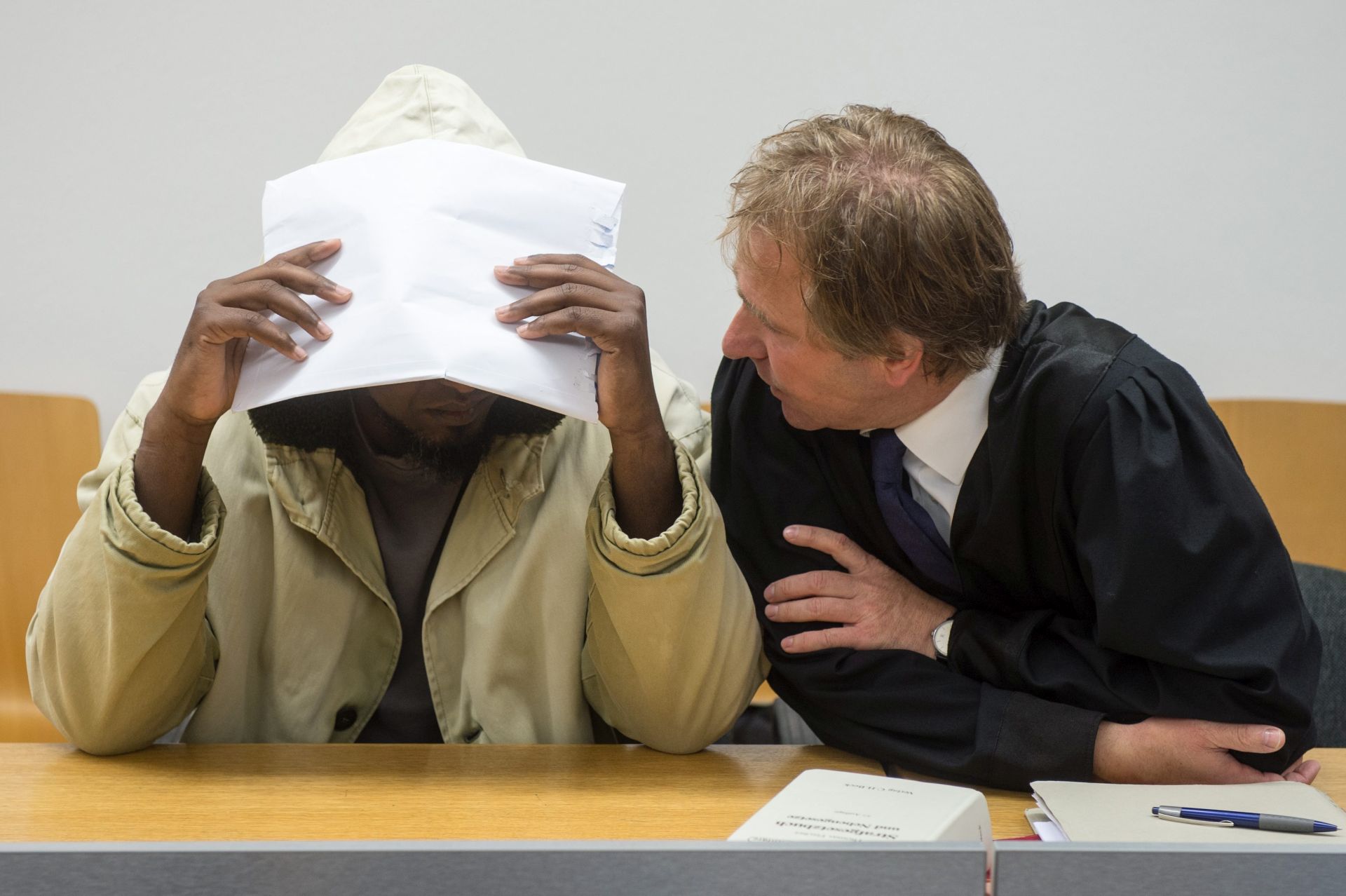 epa05467033 Defendant Mohammed S. (L) tries to cover his face as he speaks with his defense lawyer Thomas Krimmel (R) in the courtroom of the district court in Landshut, Germany, 09 August 2016. The 38-year-old man is charged with stabbing to death a 20-year-old roommate following a fight in a refugee home in February 2016.  EPA/ARMIN WEIGEL  EPA/ARMIN WEIGEL