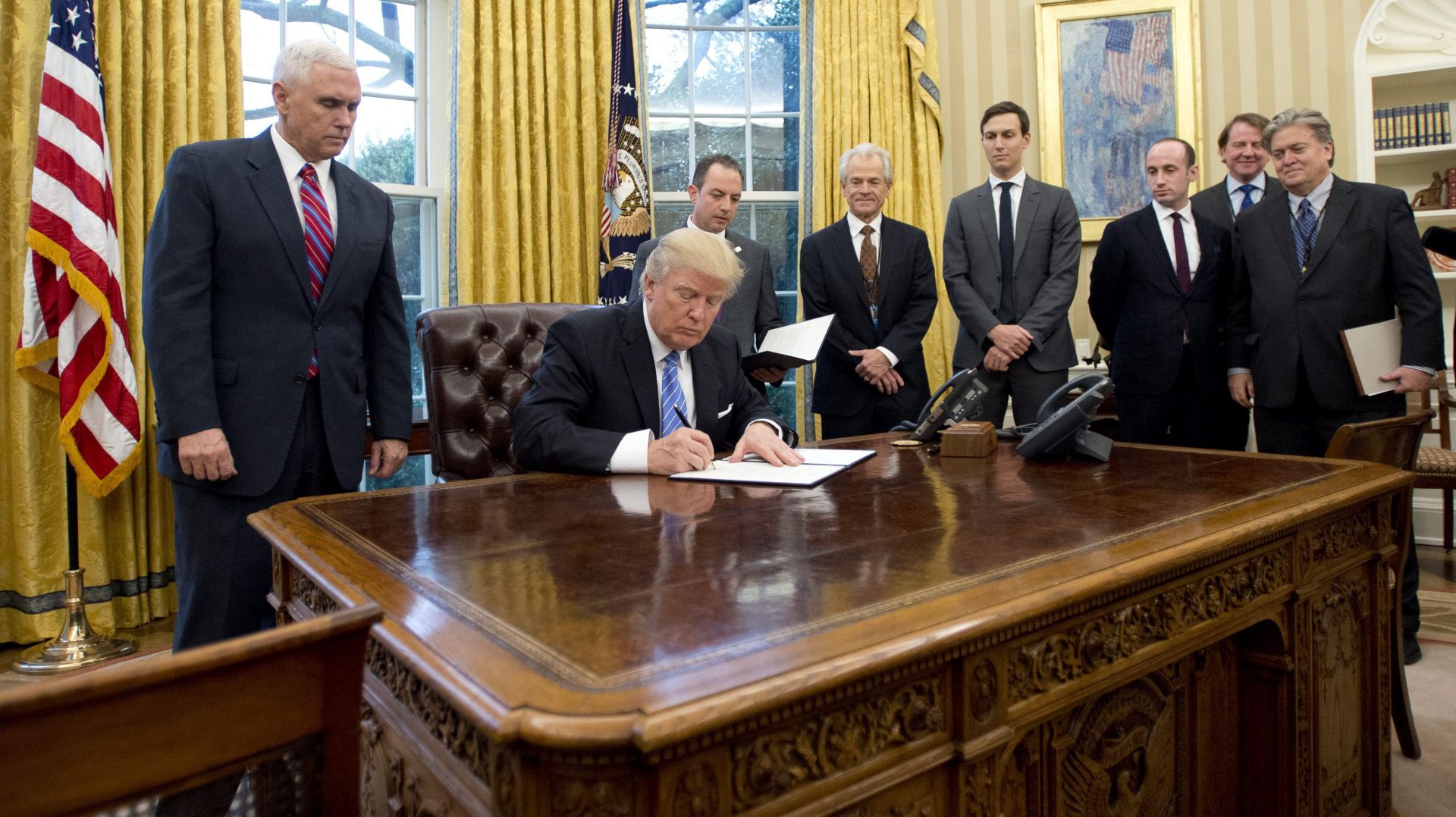 epa05744781 US President Donald J. Trump signs the first of three Executive Orders in the Oval Office of the White House in Washington, DC, USA, 23 January 2017. They concerned the withdrawal of the United States from the Trans-Pacific Partnership (TPP), a US Government hiring freeze for all departments but the military, and "Mexico City" which bans federal funding of abortions overseas. Standing behind the President, from left to right: US Vice President Mike Pence; White House Chief of Staff Reince Preibus; Peter Navarro, Director of the National Trade Council; Jared Kushner, Senior Advisor to the President; Steven Miller, Senior Advisor to the President; unknown; and Steve Bannon, White House Chief Strategist.  EPA/Ron Sachs / POOL