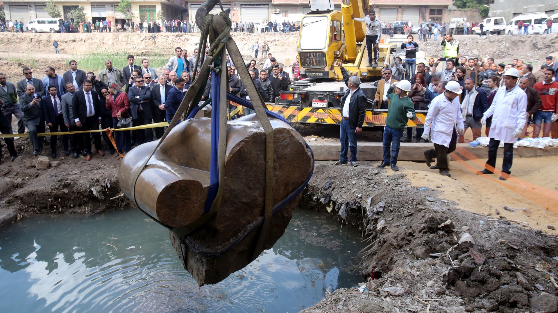 epa05845435 Egyptians look on as a crane lifts parts of a statue for restoration after it was unearthed at Souq al-Khamis district, at al-Matareya area, Cairo, Egypt, 13 March 2017. According to the Ministry of Antiquities, a German-Egyptian archaeological mission found in parts two 19th dynasty royal statues in the vicinity of King Ramses II temple in ancient Heliopolis.  EPA/KHALED ELFIQI