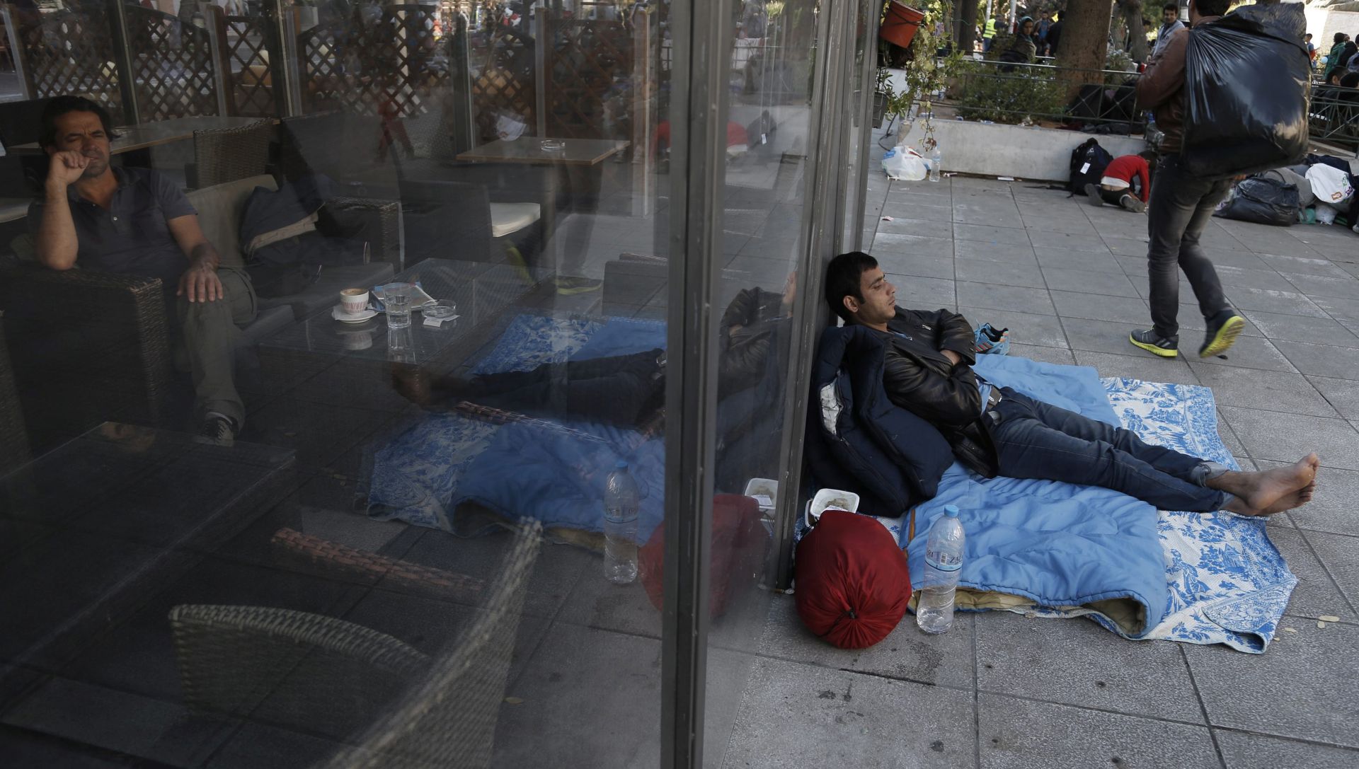 epa05019212 A customer sits in cafe as an Afghan man rests outside of it at Victoria Square, where hundreds of migrants find temporary shelter before continuing their journey to central Europe, in Athens, Greece, 10 November 2015. Europe is dealing with its greatest influx of migrants and asylum seekers since World War II as immigrants fleeing war and poverty in the Middle East, Afghanistan and Africa try to reach Germany and other Western European countries.  EPA/YANNIS KOLESIDIS