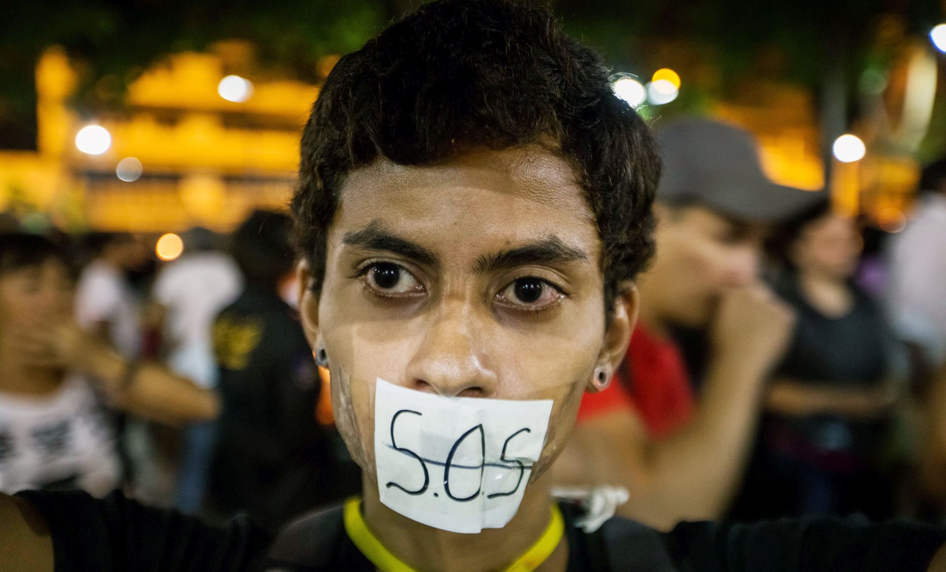epa05936379 A woman covers her mouth with a sign reading 'S.O.S.' (the international Morse code distress signal) during vigil in Caracas, Venezuela, 29 April 2017. Venezuelan students held a 12-hour vigil in honor of people whom lost their lives during the recent anti-government rallies, while opposition parties called for another march on Monday in order to call for general elections and a new Supreme Court.  EPA/MIGUEL GUTIERREZ