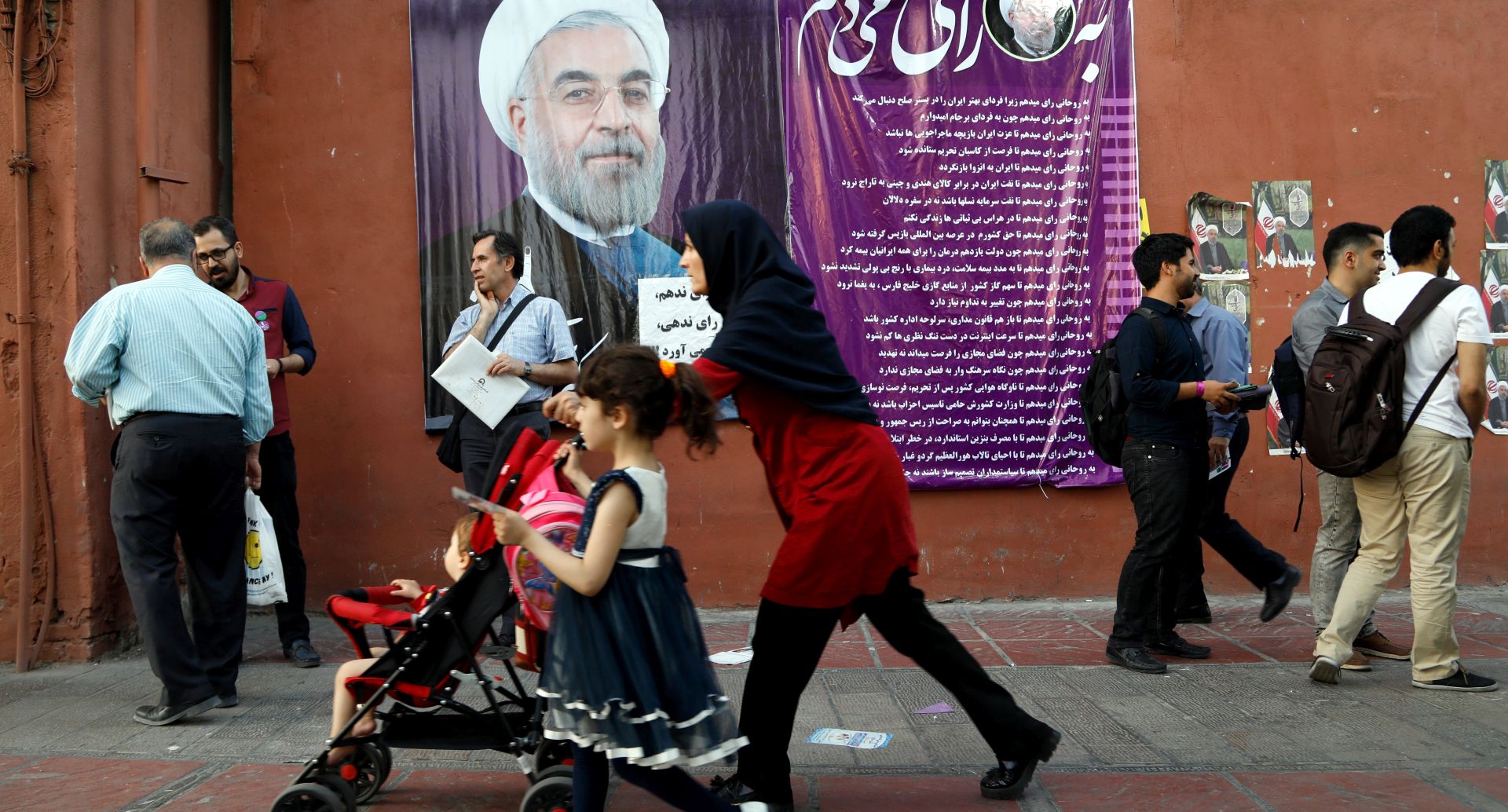 epa05966474 Iranians walk next to a huge election banner of current president and presidential candidate Hassan Rouhani at a street in Tehran, Iran, 15 May 2017. Media reported that conservative presidential candidate Ebrahim Raisi is the main contender against president Hassan Rouhani in the upcoming presidential election. Iranians will go to the poll for the presidential election on 19 May 2017.  EPA/ABEDIN TAHERKENAREH
