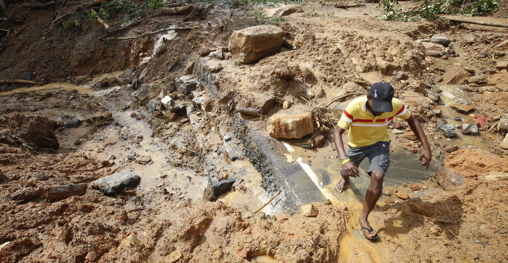 epa05994746 A road is completely damaged as a man walks past at the area where a landslide occured in which 35 people are feared killed at Athwelthote in Baduraliya, some 98 kilometers from Colombo, Sri Lanka, 28 May 2017. Following a prolonged drought Sri Lanka has been hit with the monsoonal rains for the past few days causing heavy flooding and landslides in several parts of the island including its capital Colombo. The government's Disaster Management Centre confirmed that 100 deaths have been reported while 99 are missing and over 53,000 have been displaced.  EPA/M.A.PUSHPA KUMARA