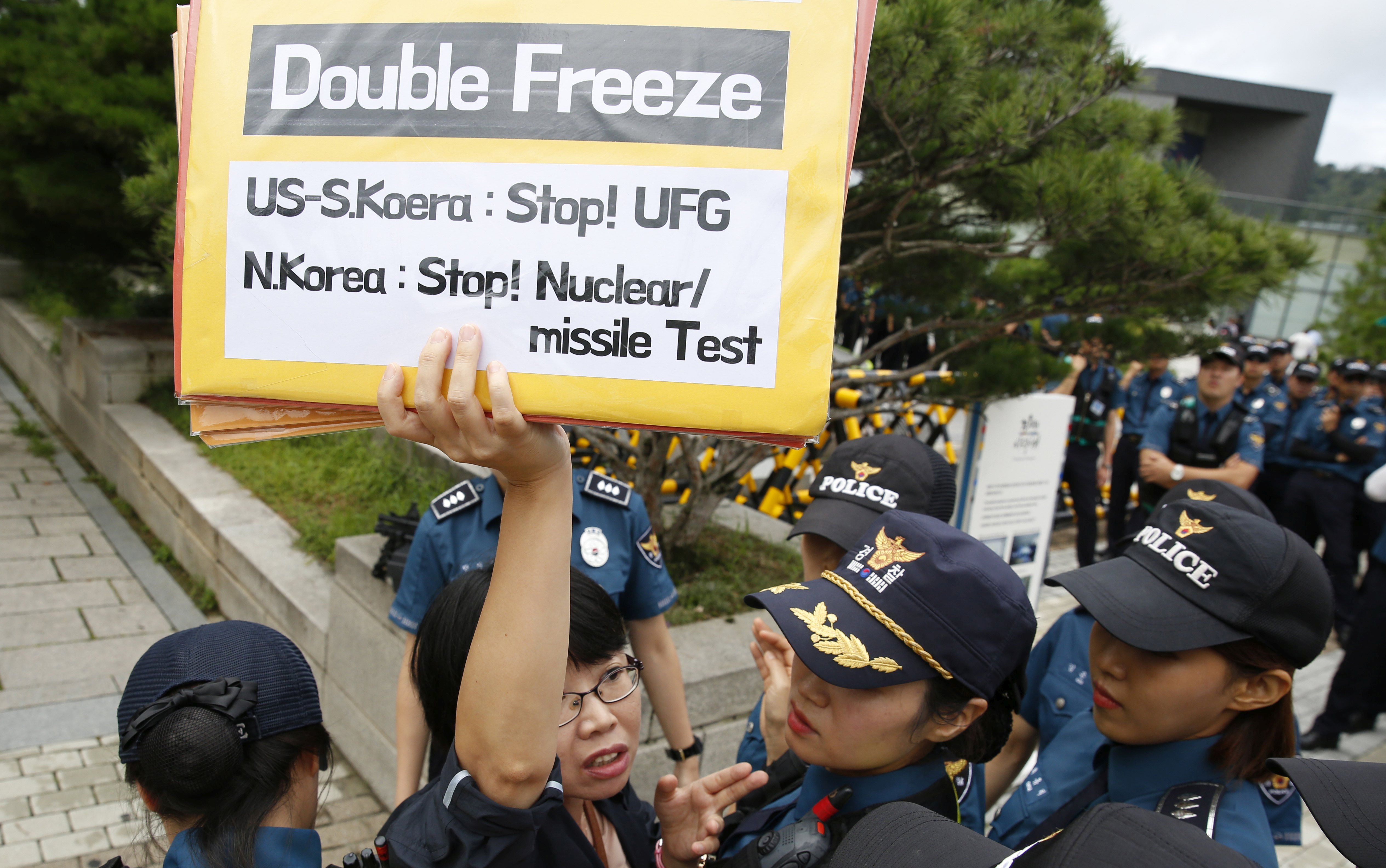 epa06154083 A South Korean protester shouts slogans and holds a placards as policemen surround her during a demonstration against South Korean and US military forces joint 'Ulchi Freedom Guardian (UFG)' exercises, near the Presidential House in Seoul, South Korea, 21 August 2017. The South Korean and US military forces joint exercise is held from 21 to 31 August, to prepare for possible North Korean attacks.  EPA/JEON HEON-KYUN