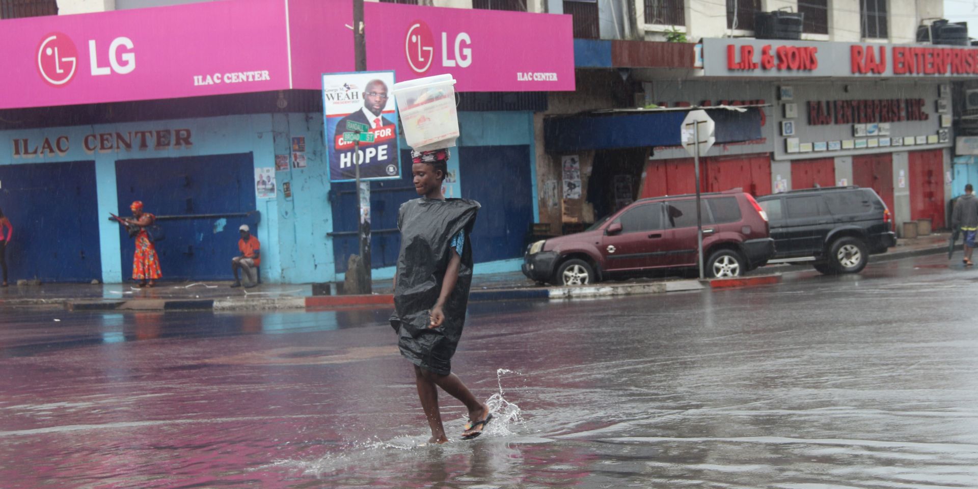 epa06181858 A woman carries a bucket on her head as she walks through  a flooded street in downtown Monrovia, Liberia 03 September 2017. According to reports torrential rains have killed, displaced, and destroyed many people and properties in some parts of West Africa, including Ghana, Niger, Nigeria, Sierra Leone and other parts of the region, due to heavy rain fall since June of this year.  EPA/AHMED JALLANZO