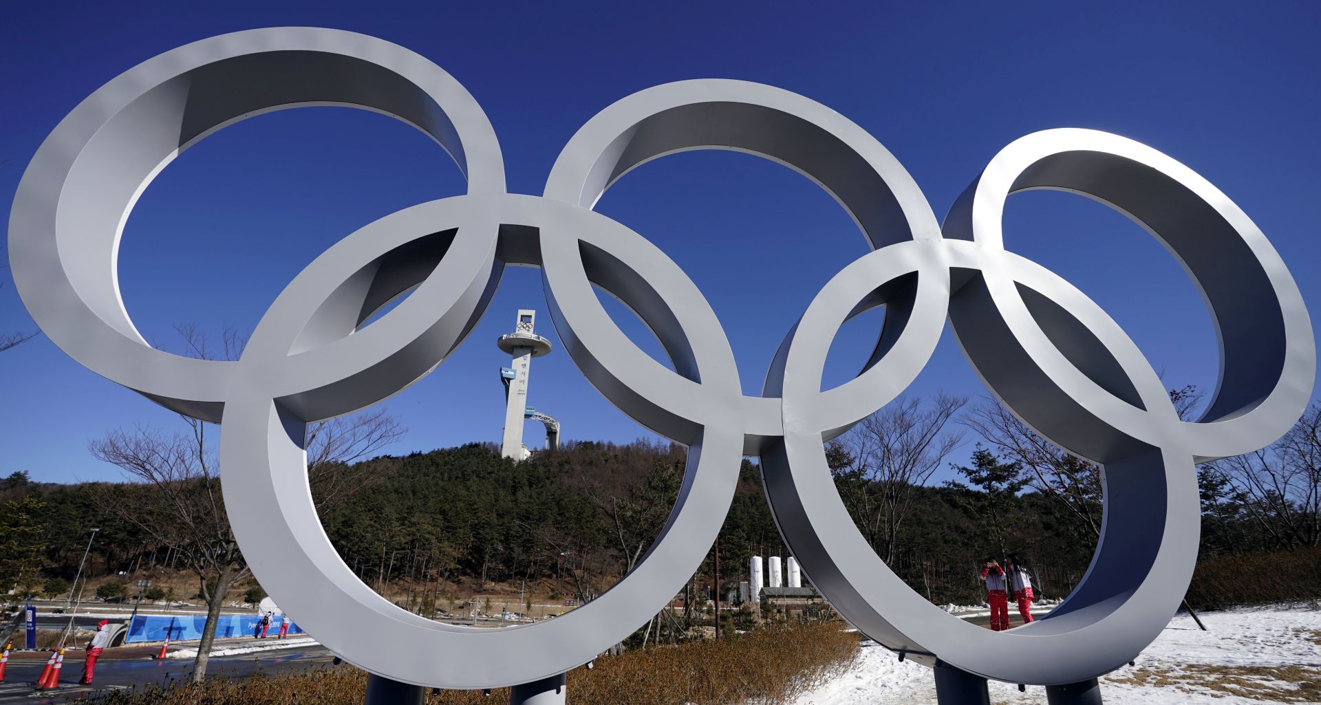 epa06489148 Volunteers pass near the Olympic rings installation (front) and the Alpensia Ski Jumping Center (back) of the PyeongChang Winter Olympic Games 2018 at the Alpensia Resort in the northeastern alpine town of PyeongChang, South Korea, 01 February 2018. The PyeongChang 2018 Winter Games Olympics, will run from 09 to 25 February 2018.  EPA/SERGEI ILNITSKY