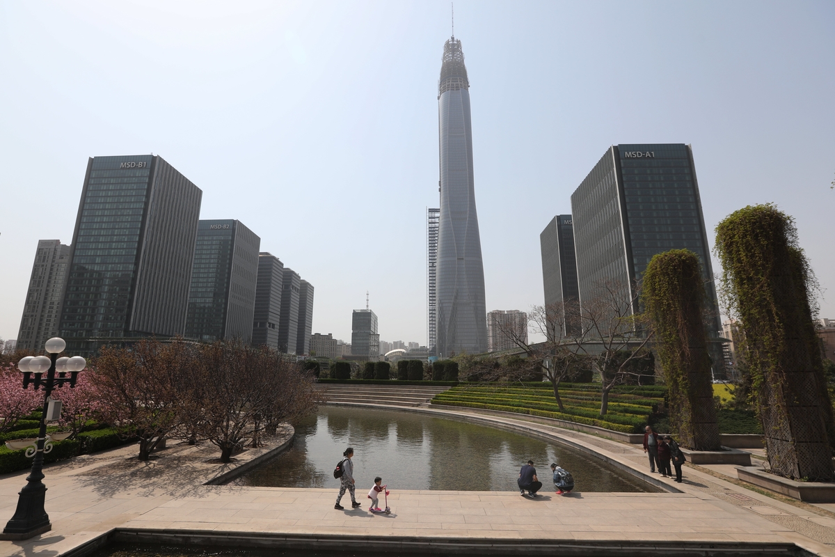 epa06674076 Chinese citizens walk through a park near the unfinished 530-meter-high Tianjin CTF Finance Centre (C, back) in Tianjin, China, 17 April 2018. China's gross domestic product (GDP) grew 6.8 percent in the first quarter of 2018, according to a report from China's National Bureau of Statistics on 17 April 2018.  EPA/WU HONG