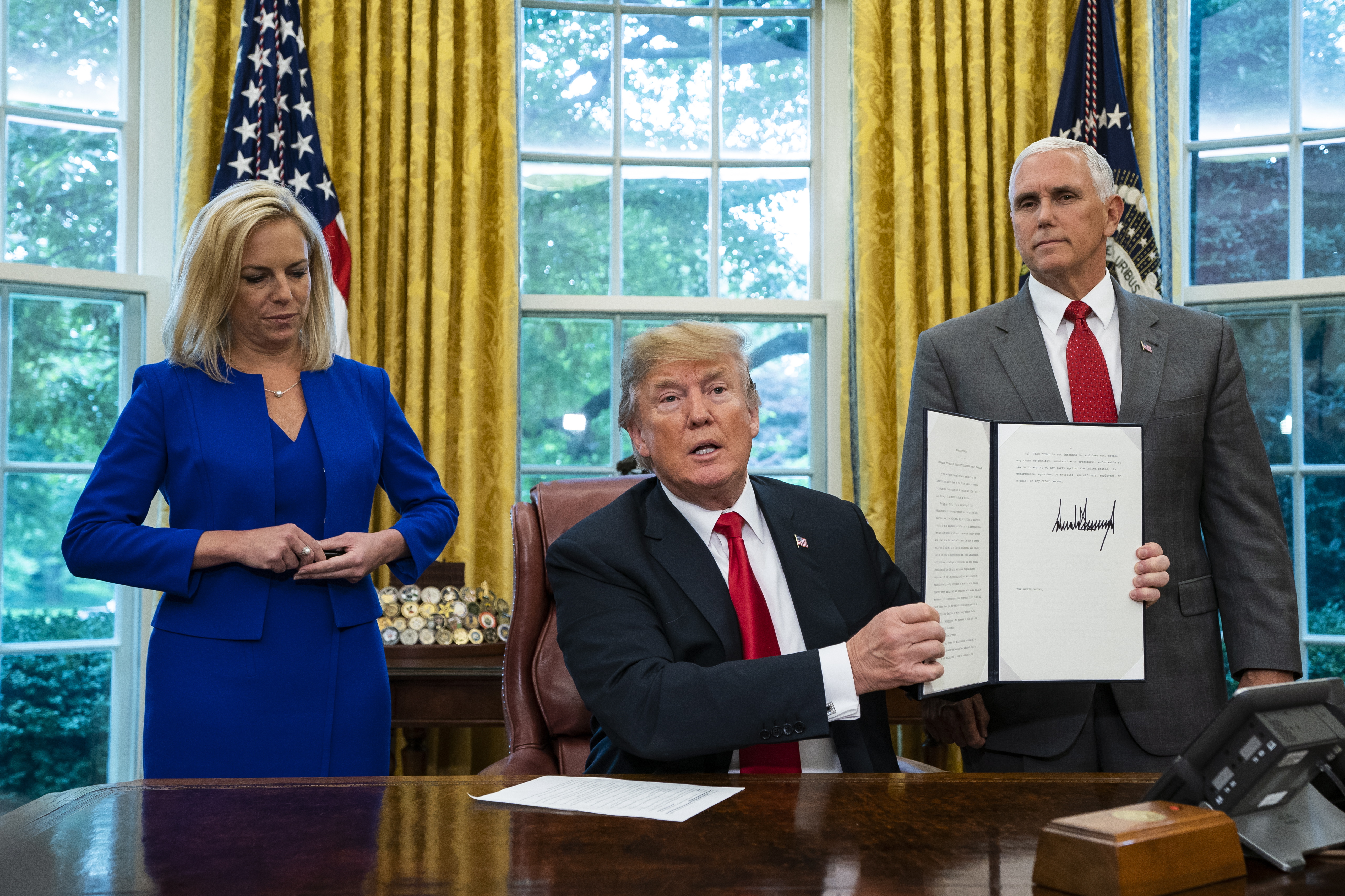 epa06825657 US President Donald J. Trump (C), flanked by Homeland Security Secretary Kirstjen Nielsen (L) and Vice President Mike Pence (R), holds an executive order he signed to stop migrant children from being separated from their parents at the US border in the Cabinet Room of the White House Washington, DC, USA 20 June 2018.  The Trump administration was facing bipartisan criticism for its 'zero tolerance' policy at the border, which resulted in the separations.  EPA/JIM LO SCALZO