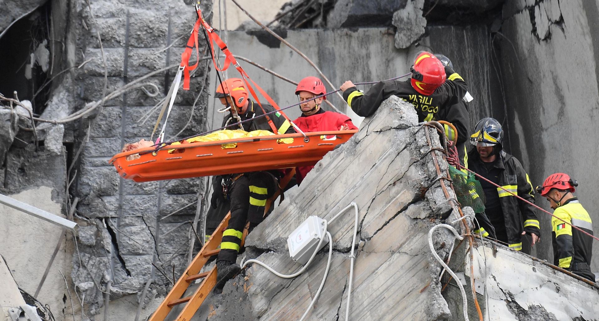 epa06949717 Rescuers recover an injured person after a highway bridge collapsed in Genoa, Italy, 14 August 2018. At least 22 people are believed to have died as a large section of the Morandi viaduct upon which the A10 motorway runs collapsed in Genoa on Tuesday. Both sides of the highway fell. Around 10 vehicles are involved in the collapse, rescue sources said. The viaduct gave way amid torrential rain.  EPA/LUCA ZENNARO
