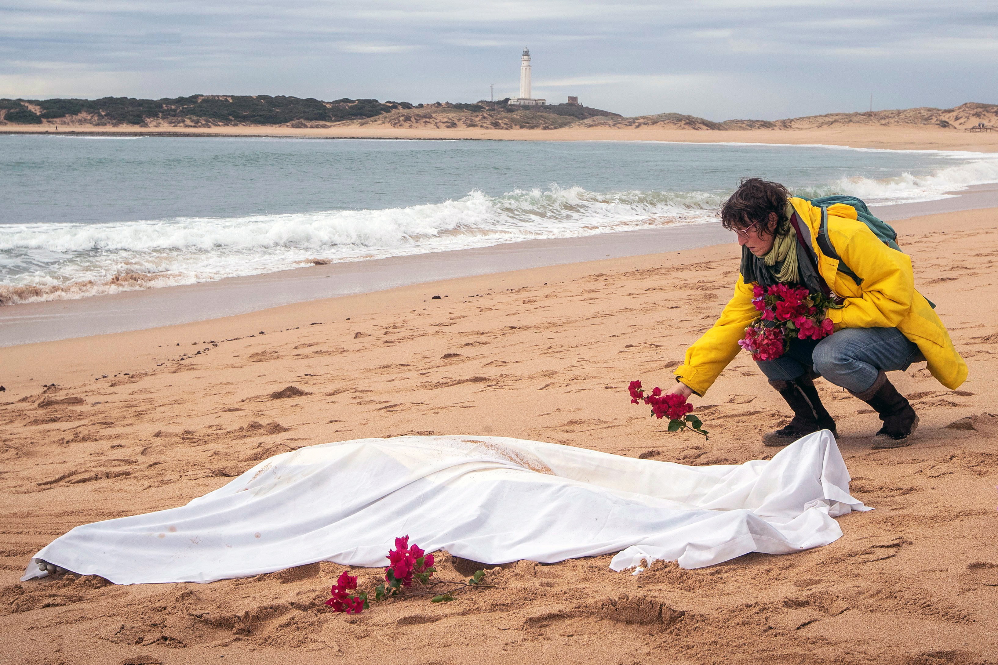 epa07161087 A woman lays flowers around the body of a migrant found in Canos de Meca beach in Cadiz, southern Spain, 12 November 2018. A total of 17 dead migrants were found so far, after the bodies of two of them were found in the past few hours. The migrants died after their boat sunk on 05 November 2018.  EPA/ROMAN RIOS