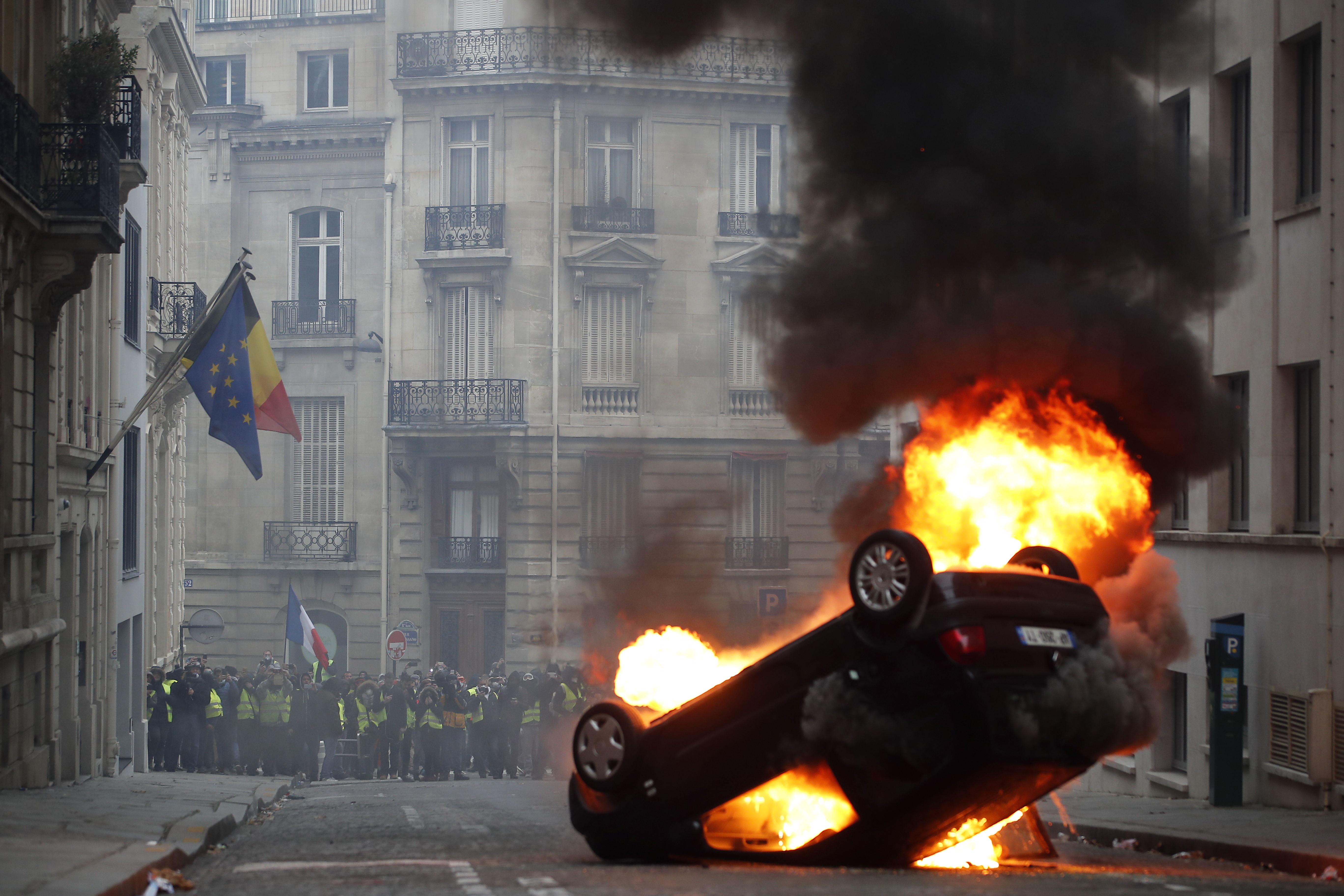 epa07217247 Yellow Vests (Gilets jaunes) protesters are seen behind a burning overturned car near Avenue Marceau during the  demonstration in Paris, France, 08 December 2018. The so-called 'gilets jaunes' (yellow vests) is a protest movement, which reportedly has no political affiliation, that continues protests across the nation over high fuel prices.  EPA/IAN LANGSDON