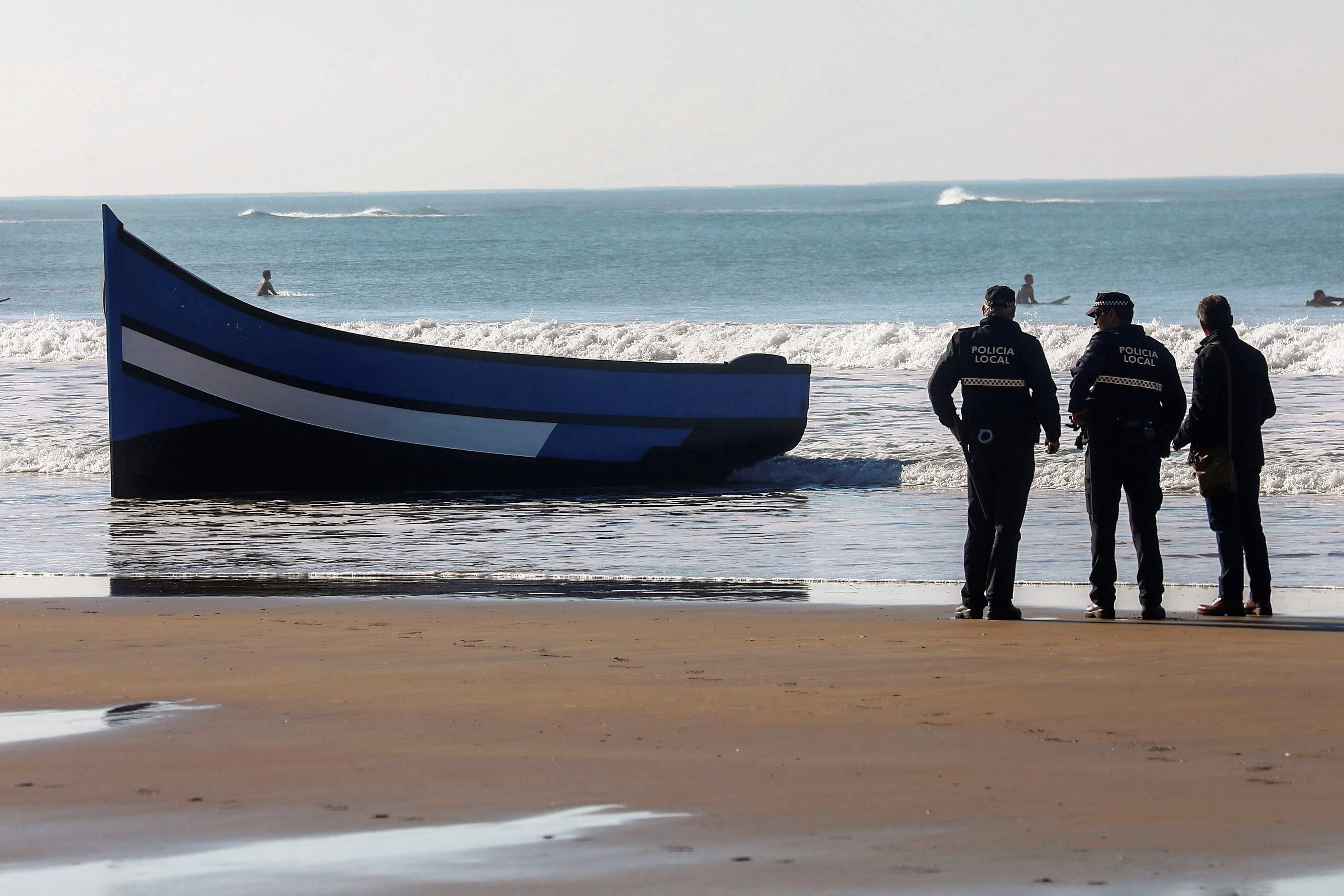 epa07219123 Local policemen stand guard next to a boat in which a total of 30 migrants managed to reach Santa Maria del Mar beach in Cadiz, southern Spain, 09 December 2018. Spanish authorities reported that the police was alerted by residents after all the migrants, from Maghreb, began to run away when they got ashore. The authorities have detained 18 people of them, so far.  EPA/Roman Rios