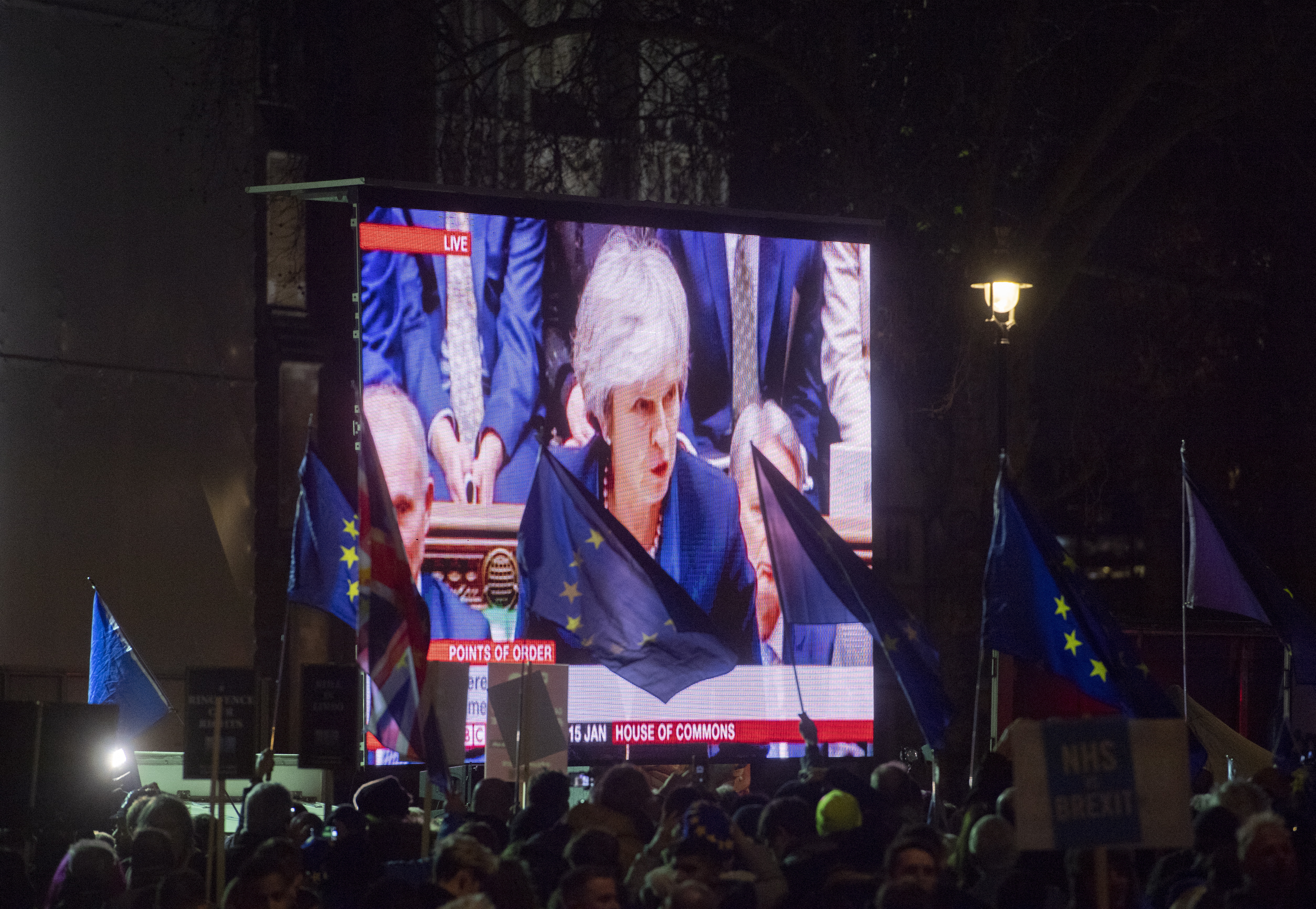 epa07287891 Protesters' flags flutter as Britain's Prime Minister Theresa May makes a statement on a video screen outside the Houses of Parliament after being defeated in the vote on Brexit EU Withdrawal Agreement in London, Britain, 15 January 2019. Parliamentarians voted on the postponed Brexit EU Withdrawal Agreement, commonly known as The Meaningful Vote, deciding on Britain's future relationship with the European Union.  EPA/FACUNDO ARRIZABALAGA