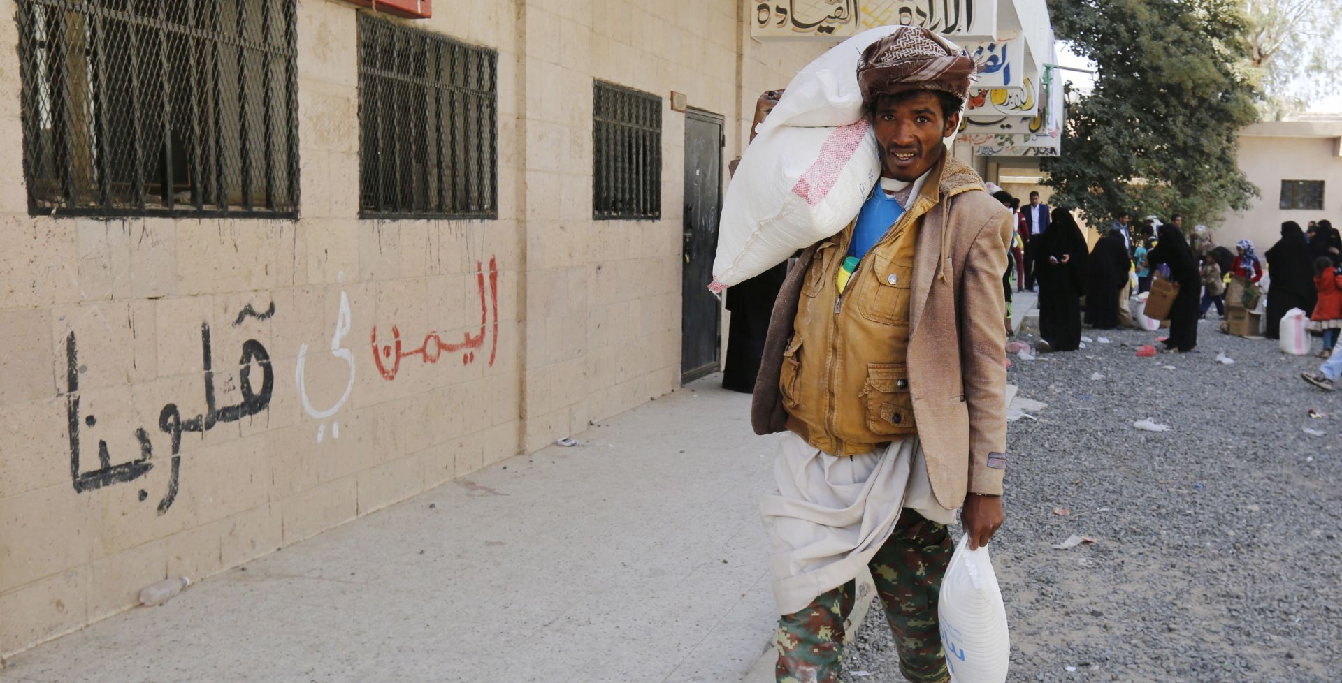 epa07373128 A conflict-affected Yemeni man passing a building with the words in Arabic ‘Yemen is in our hearts’ carries food rations provided by Mona Relief Yemen at a neighborhood in Sana'a, Yemen, 14 February 2019 (issued 15 February 2019). According to reports, the United Nations has warned that the situation in war-torn Yemen is getting even worse as a four-year long conflict between the Saudi-backed government forces and the Houthi rebels has created the worst humanitarian crisis in the world, where some 80 percent of Yemen's 26-million population are in need of humanitarian assistance.  EPA/YAHYA ARHAB