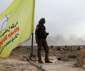 epa07461235 A Fighter of the Syrian Democratic Forces (SDF) stands guard next to the yellow flag of US-backed Syrian Democratic Forces (SDF) atop a building in the village of Baghuz, Syria, 24 March 2019. The US-backed Kurdish-Arab 'Syria democratic forces' (SDF) have announced the military victory over Islamic State (IS) group on 23 March 2019, following a four-year battle against the group that took control over a third of Syria and Iraq.  EPA/Ahmed Mardnli