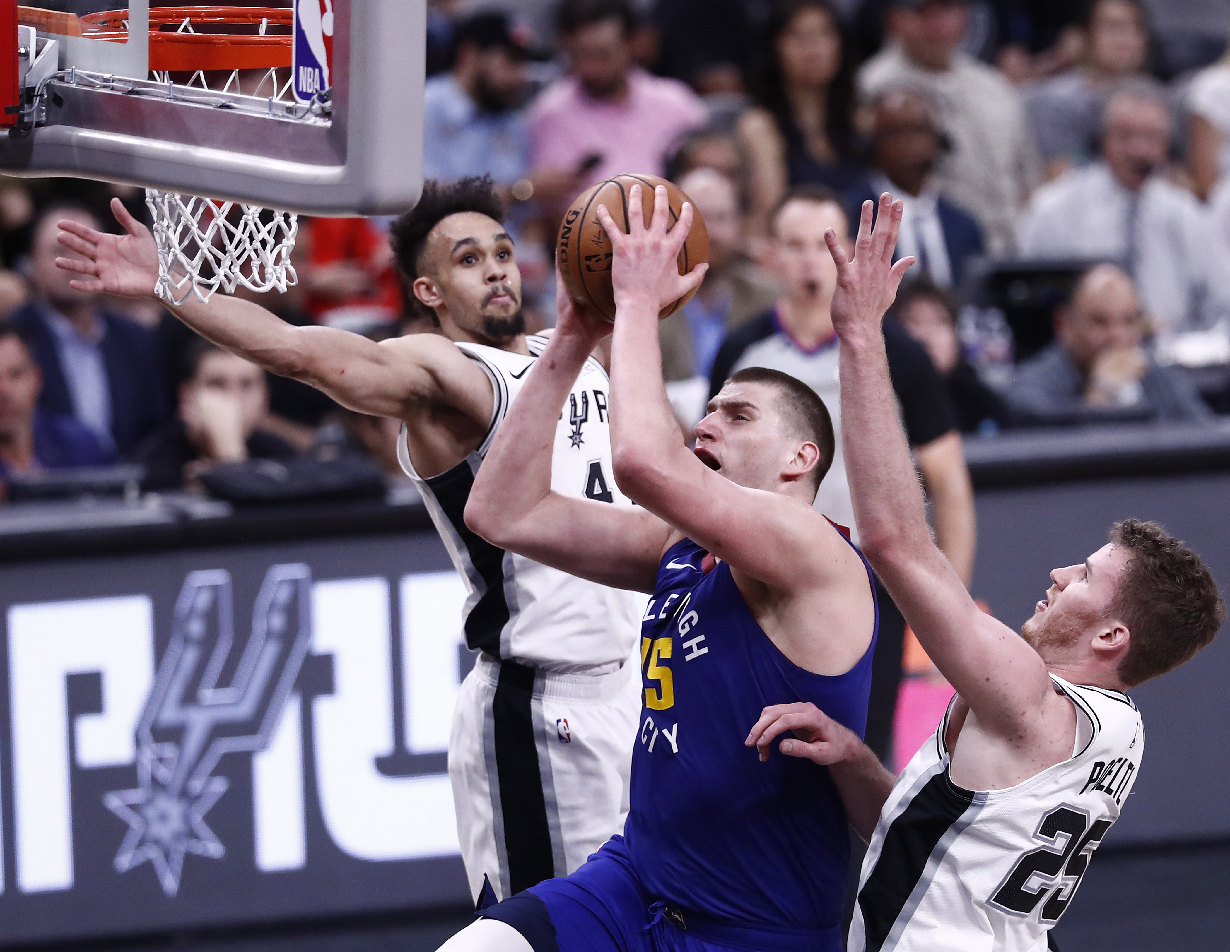 epa07528825 Denver Nuggets player Nikola Jokic of Serbia (C) goes to the basket against San Antonio Spurs players Derrick White (L) and Jakob Poeltl of Austria (R) during the NBA Western Conference Playoffs game six at the AT&T Center in San Antonio, Texas, USA, 25 April 2019.  EPA/LARRY W. SMITH SHUTTERSTOCK OUT