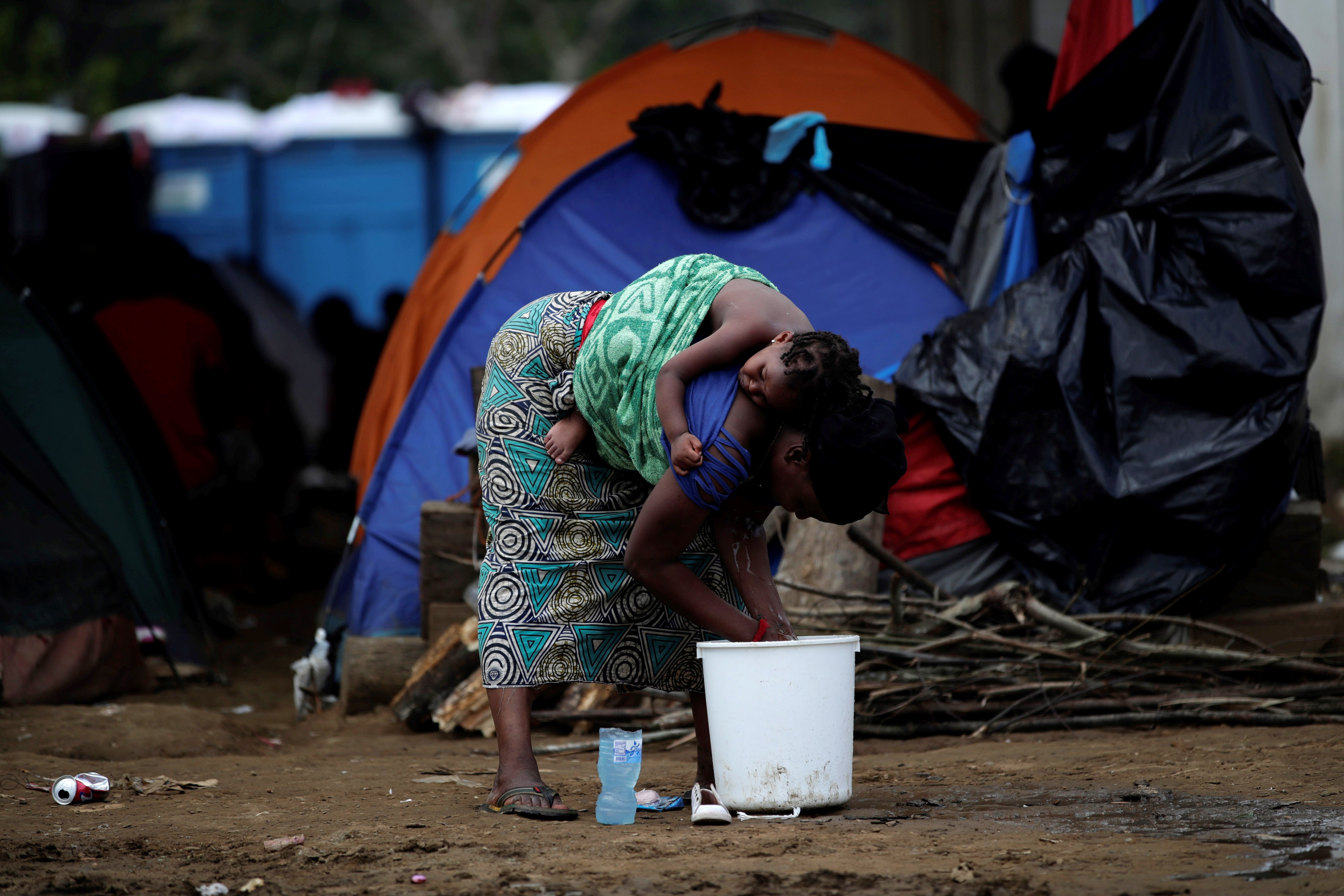 epa07611568 (17/40) A migrant woman carries her child her back while doing the dishes at a temporary humanitarian campsite in the village of Penita, Darien, Panama, 22 May 2019. Every week, hundreds of migrants arrive on small boats to Penita, a small indigenous village in the Darien Gap on the Panamanian side of the border with Colombia, as they make their way along a perilous route towards North America.  EPA/Bienvenido Velasco  ATTENTION: For the full PHOTO ESSAY text please see Advisory Notice epa07611551