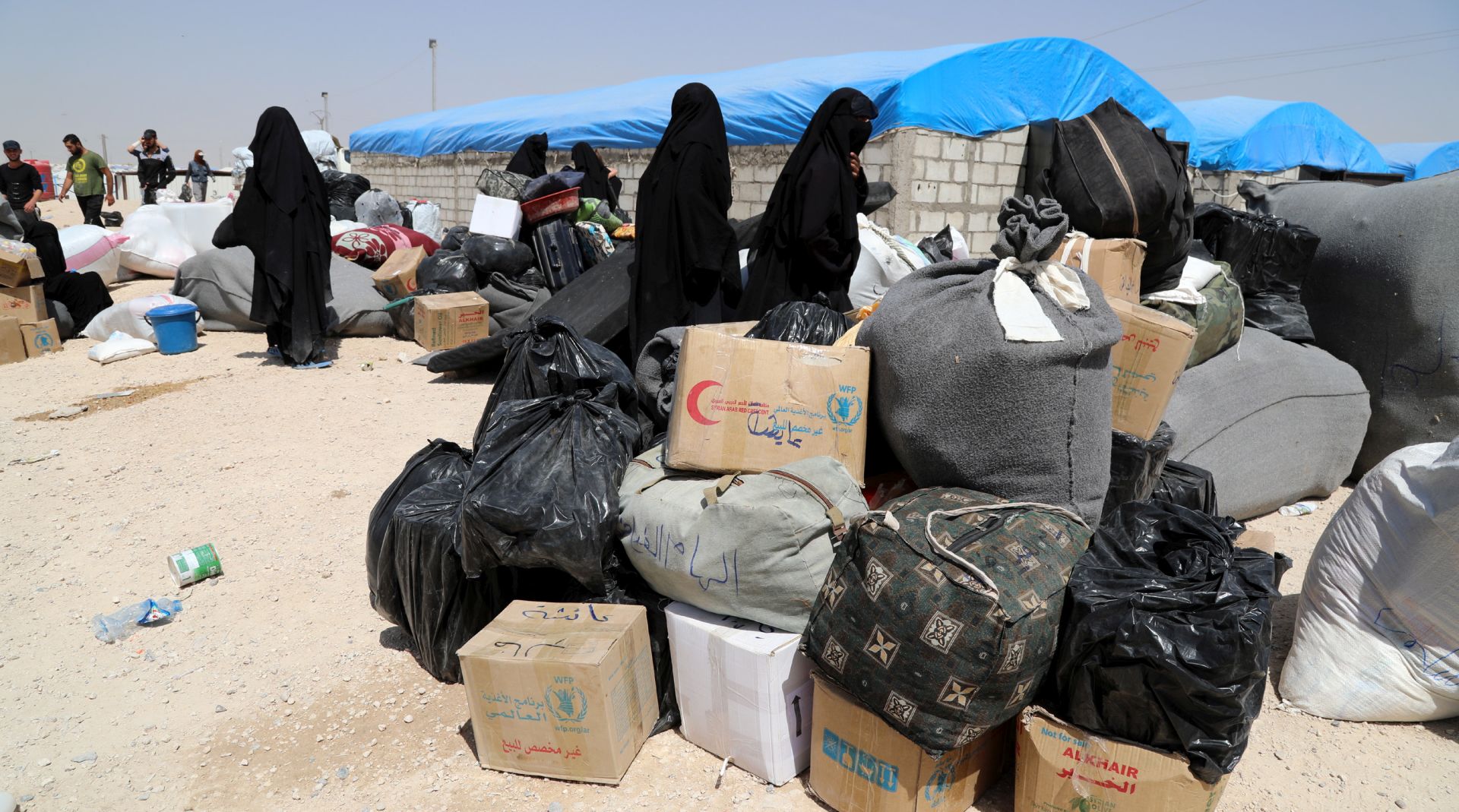 epa07623496 Wives of Islamic state fighters (IS) wait next to their belongings upon their deportation from the al-Hol camp for refugees in al-Hasakah governorate in northeastern Syria on 03 June 2019 (issued 04 June 2019).  According to media reports, the Kurdish authorities in northeast Syria are handing over 800 women and children all of them Syrian, including relatives of Islamic state fighters, to their families in the first such transfer from an overcrowded camp.  EPA/AHMED MARDNLI