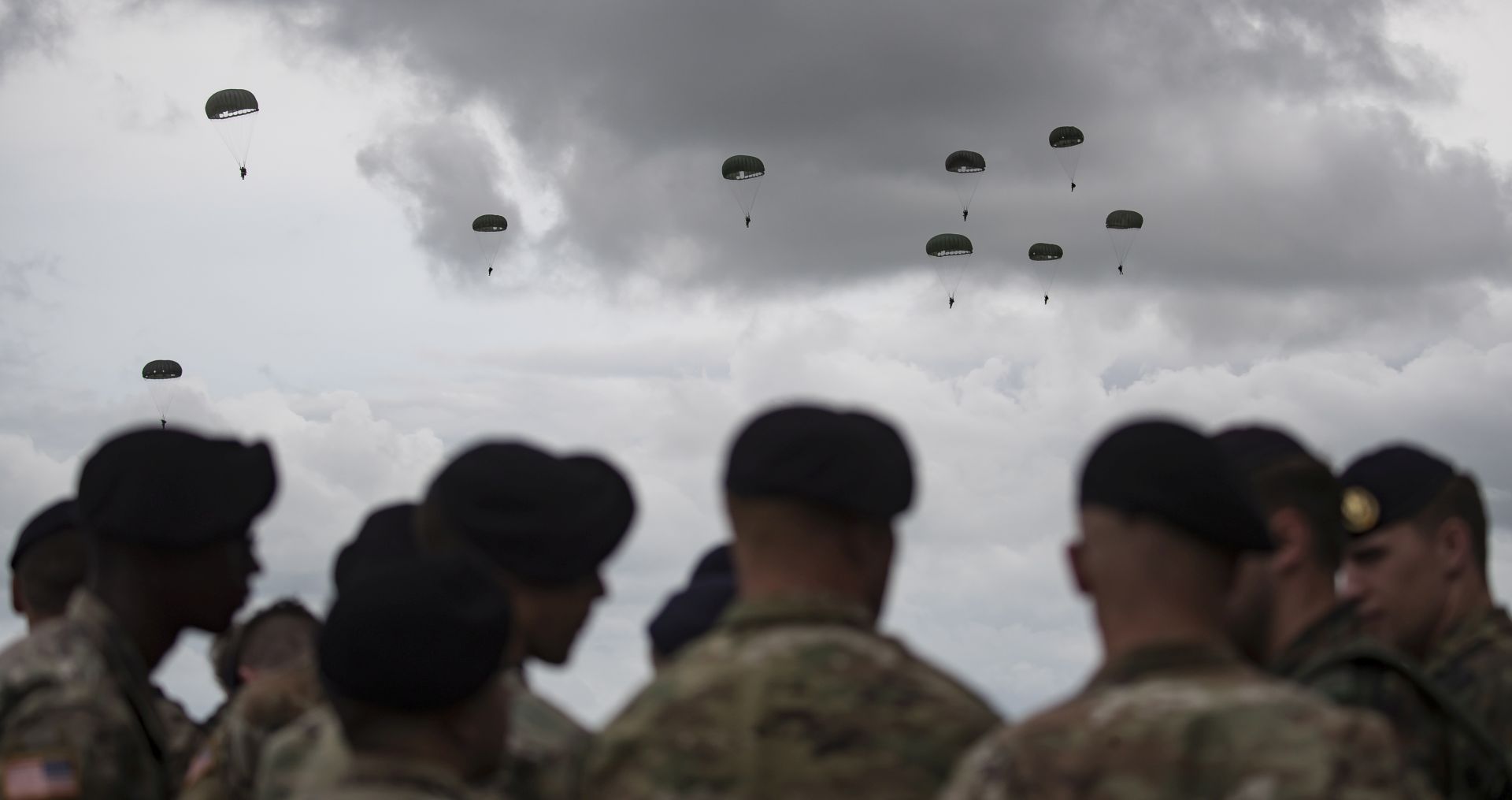epa07627006 US Airborne soldiers look on as C-47 Dakota airplanes drop parachutists in WW2 attire near the Normandy coast ahead of the 75th D-Day anniversary, in Carentan,  France, 05 June 2019. World leaders are to attend memorial events in Normandy, France on 06 June 2019 to mark the 75th anniversary of the D-Day landings, which marked the beginning of the end of World War II in Europe.  EPA/IAN LANGSDON