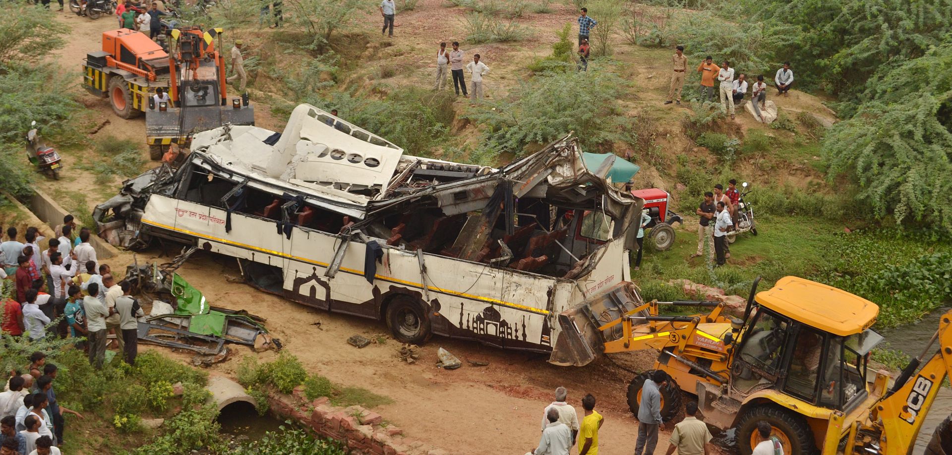 epa07702732 People gather around a damaged bus at the site of an accident where the bus fell into a deep drain on Yamuna Expressway near Agra, Uttar Pradesh, India, 08 July 2019. At least 29 people, including a child and a woman, died in the accident after the bus slipped off and fell into a drain.  EPA/STR