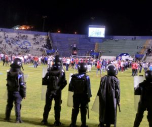 epa07778805 Supporters enter the field and protect themselves from tear gas released by authorities, due to riots outside the National Stadium, due to cancellation of the classic soccer match between teams Olimpia and Motagua in Tegucigalpa, Honduras, 17 August 2019. At least three players, including Paraguayan Roberto Moreira and Argentine Jonathan Rougier, were slightly injured on Saturday in an attack on the bus of the Honduran team Motagua before the match corresponding to the fifth day of the AperturaTournament.  EPA/STR