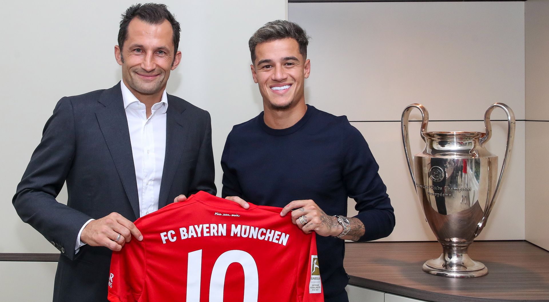 epa07780287 A handout photo made available by  FC Bayern Munich on 19 August 2019 shows Bayern's director of sport Hasan Salihamidzic (L) and Bayern's new player Philippe Coutinho from Brazil posing with Coutinhos's jersey next to the UEFA Champions League trophy in Munich, Germany, 18 August 2019. Coutinho will be presented oficcialy in the afternoon of 19 August 2019 in Munich.  EPA/HANDOUT  HANDOUT EDITORIAL USE ONLY/NO SALES