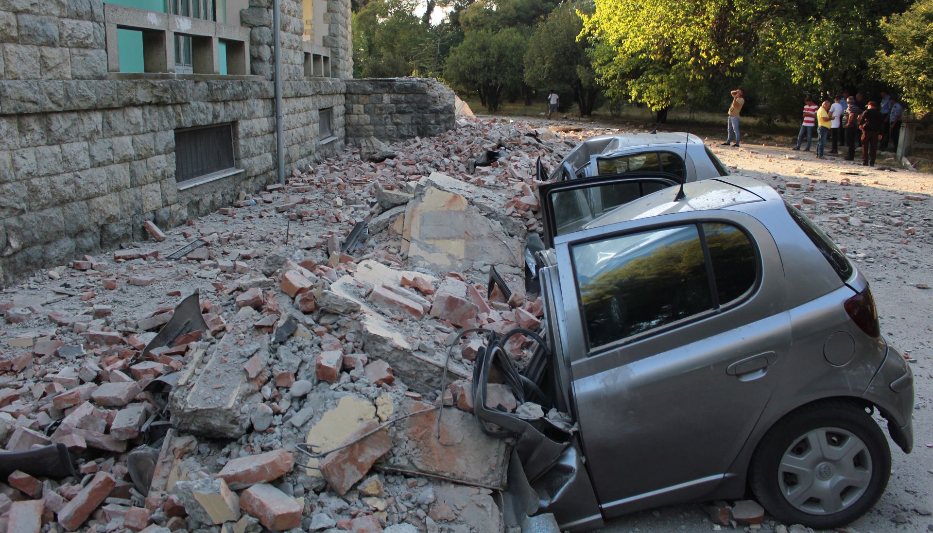 epa07859750 Locals stand at a safe area to watch the damages of crushed cars next to a building of the University of Geology and Mine, after a 5.8 magnitude earthquake hit in Tirana, Albania, 21 September 2019. According to reports, Albania was rocked by its strongest earthquake in 30 years, with the epicentre in the coastal town of Durres, at least 49 people have been reported injured from the earthquake.  EPA/MALTON DIBRA