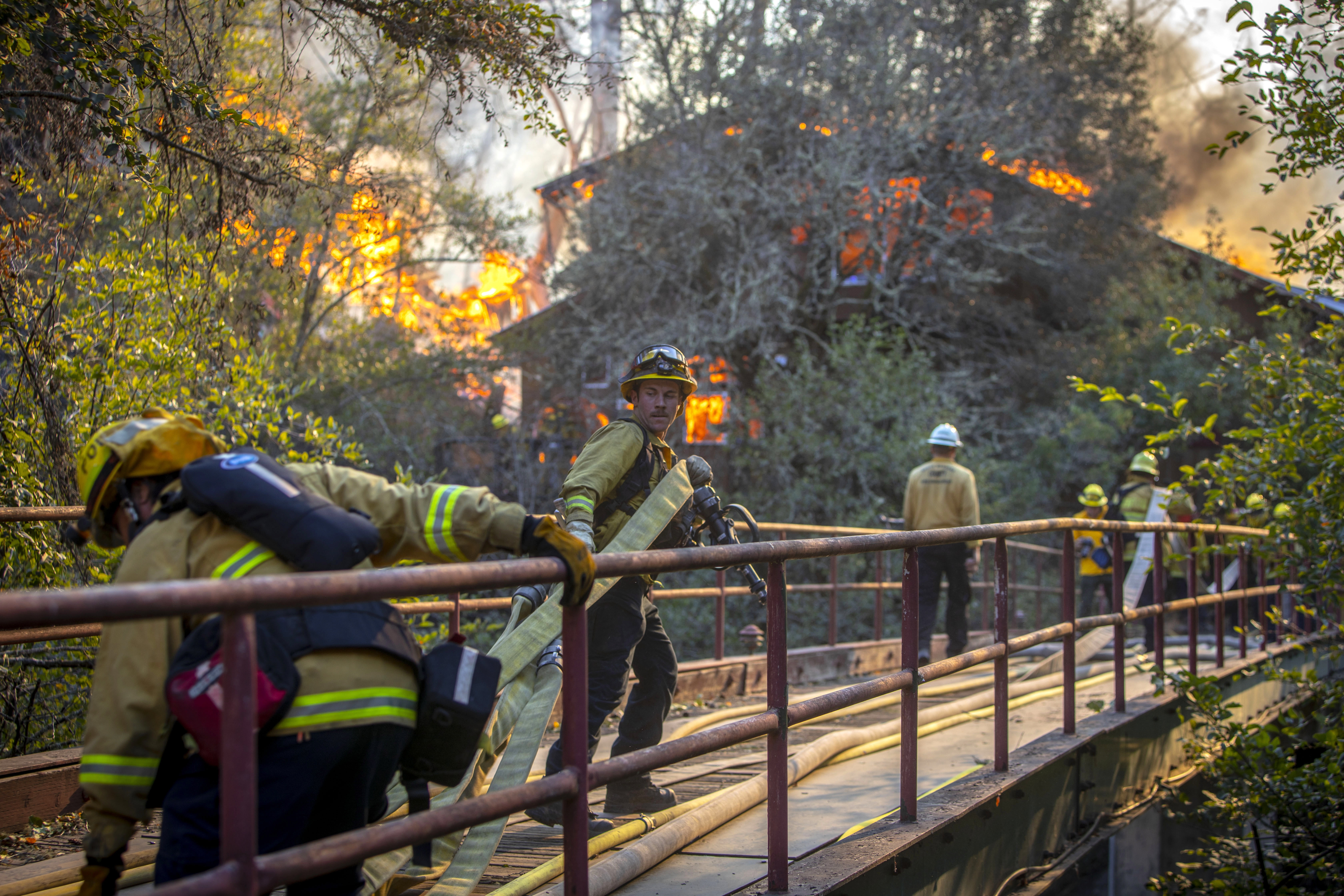 epa07958899 Firefighters navigate across a narrow bridge to battle a house fire along Hwy 128, as spot fires from the Kincade Fire erupt behind the main fire lines as a wind event starts to ramps up for the evening in Sonoma County, California, USA, 29 October 2019. The Kincade Fire has burned 75 thousand acres, destroyed over 90 buildings and is only 15 percent contained.  EPA/PETER DASILVA