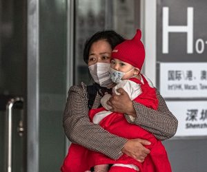 epa08300650 A woman carries a child wearing a protective face mask at the Capital International Airport, in Beijing, China, 17 March 2020. According to media reports, Beijing enforced a 14-day quarantine on international travellers arriving in China's capital. All passengers arriving from abroad go through the screening at the transfer center from where most of them are transferred in designated quarantine facilities.  EPA/ROMAN PILIPEY