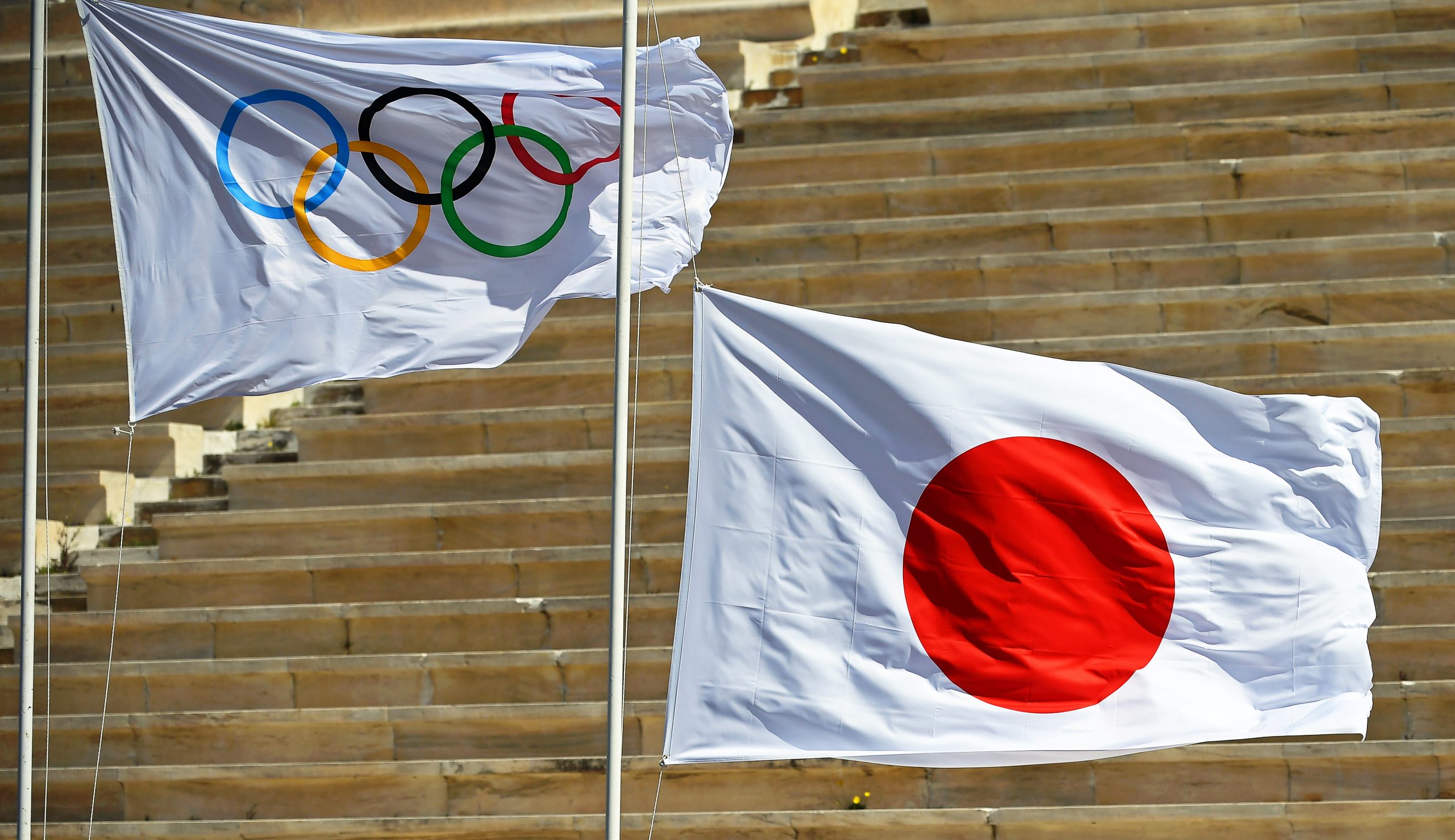 epa08306026 The national flag of Japan (R) is hoisted next to the Olympic flag (L) during the Olympic Flame handover ceremony for the Tokyo 2020 Summer Olympic Games at the Panathenaic Stadium in Athens, Greece, 19 March 2020.  EPA/ARIS MESSINIS / POOL