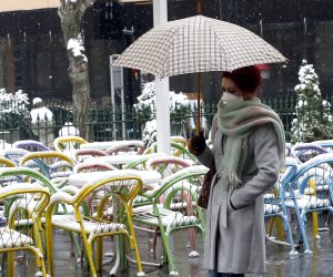 epa08318375 A woman wearing a face mask holds up an umbrella to shield herself from heavy snowfall in Sarajevo, Bosnia and Herzegovina, 24 March 2020. Several European countries have closed borders, schools, public facilities, and have canceled most major sports and entertainment events, in order to prevent the spread of the SARS-CoV-2 coronavirus, which causes the COVID-19 disease.  EPA/FEHIM DEMIR