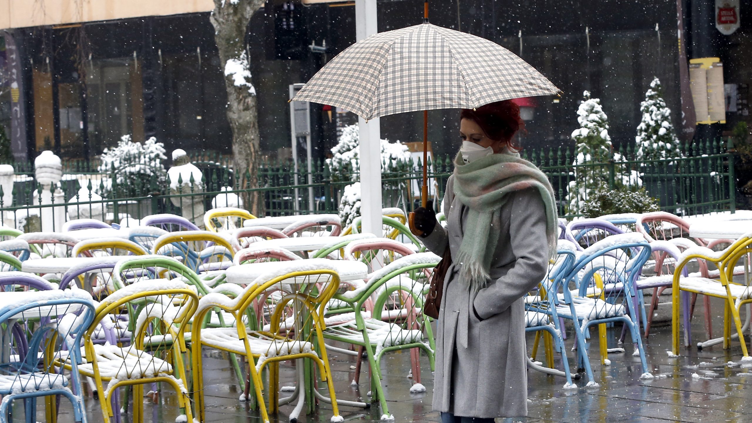 epa08318375 A woman wearing a face mask holds up an umbrella to shield herself from heavy snowfall in Sarajevo, Bosnia and Herzegovina, 24 March 2020. Several European countries have closed borders, schools, public facilities, and have canceled most major sports and entertainment events, in order to prevent the spread of the SARS-CoV-2 coronavirus, which causes the COVID-19 disease.  EPA/FEHIM DEMIR