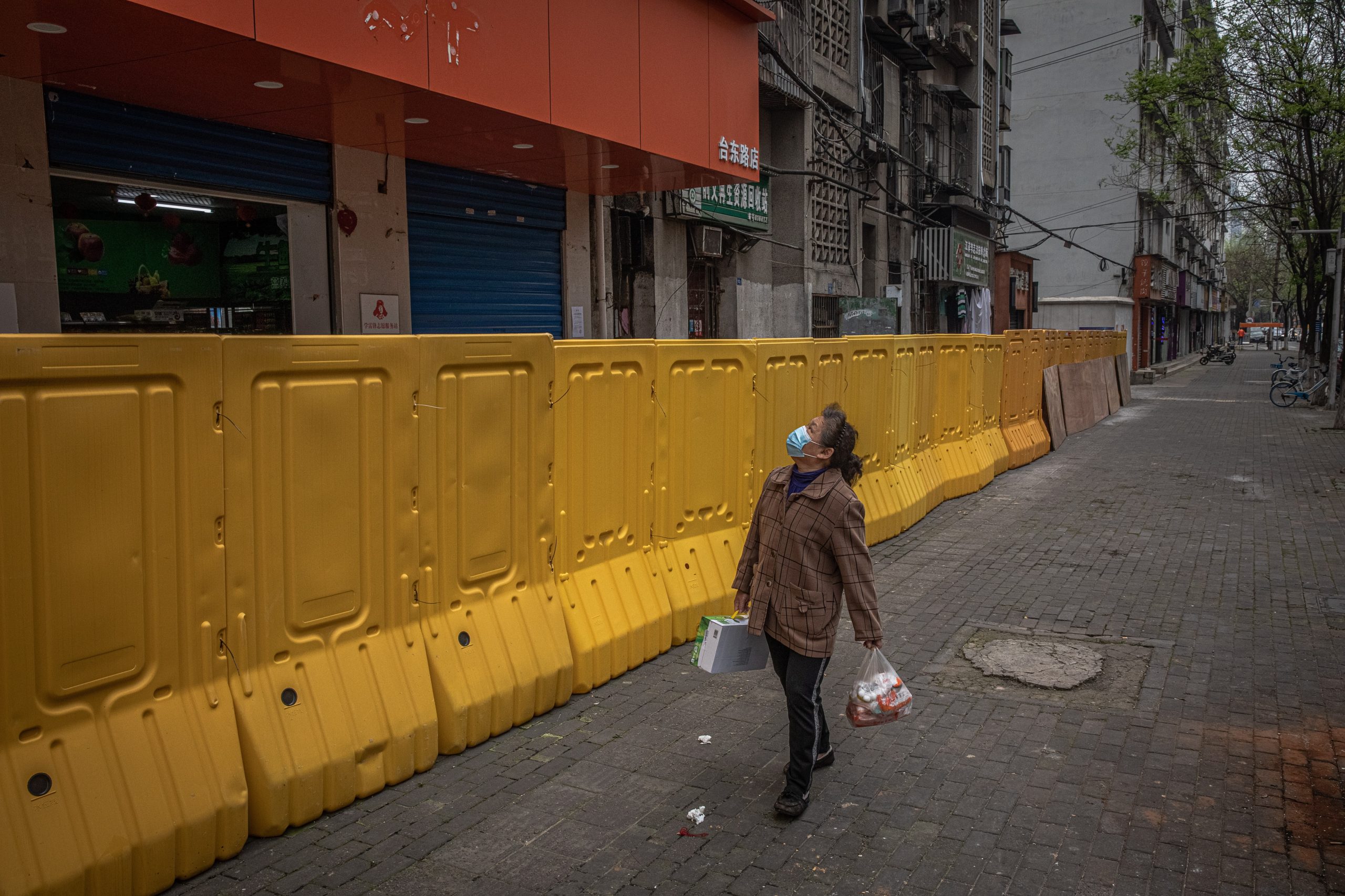 epa08354679 A woman wearing a protective face mask walks next to a security fence separating a residential area from a street, in Wuhan, China, 10 April 2020. Wuhan, the epicenter of the coronavirus outbreak, lifted the lockdown on 08 April 2020, allowing people to leave the city after more than two months.  EPA/ROMAN PILIPEY