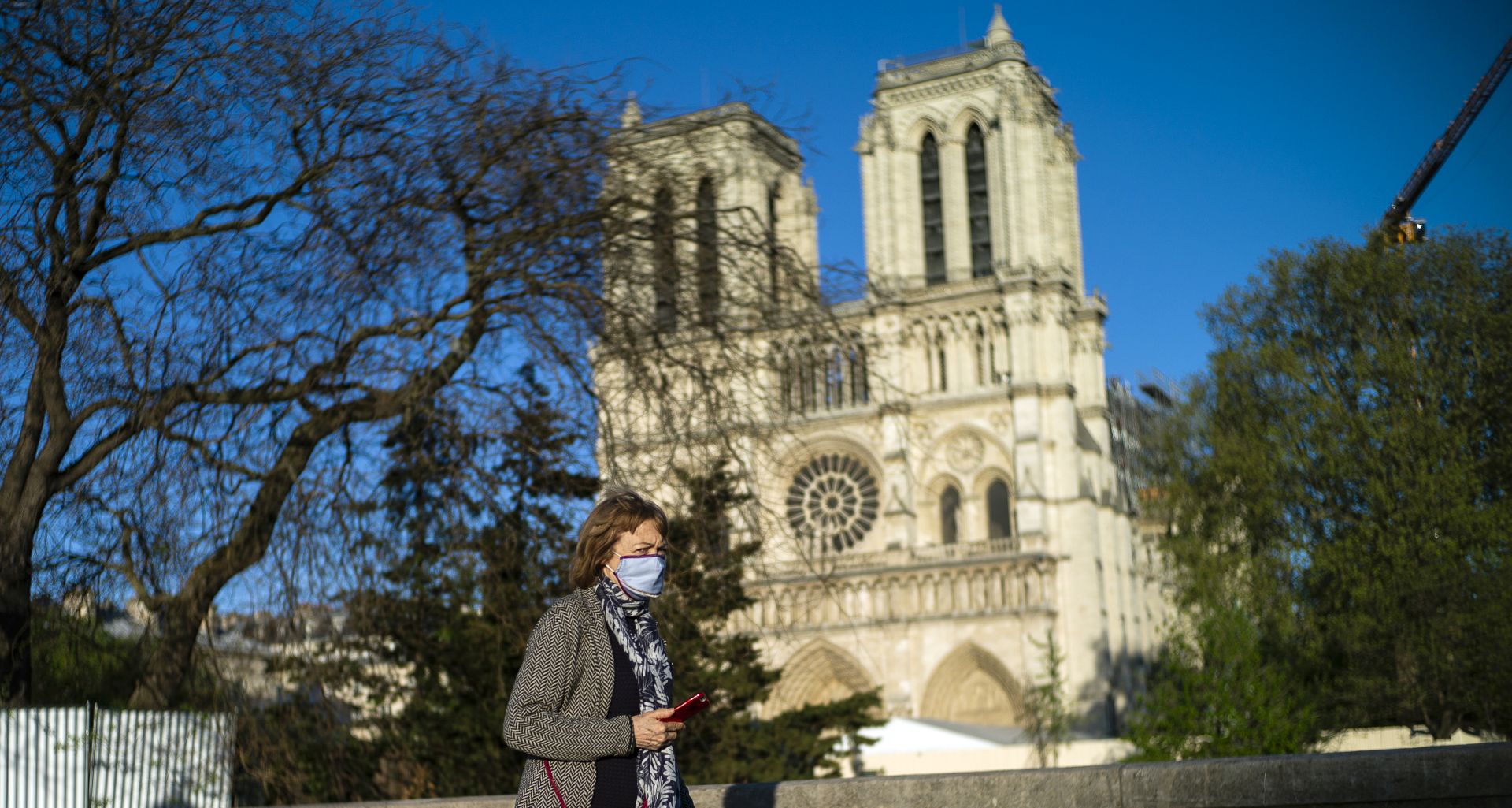 epa08365088 A woman wearing a protective face mask walks in front of the Notre-Dame cathedral on the first anniversary of the Notre-Dame fire in Paris, France, 15 April 2020. A year ago, on 15 April 2019, the 850-year-old Notre-Dame Cathedral of Paris suffered a devastating fire. Some 500 firefighters managed to prevent the entire cathedral from being reduced to ashes, although its celebrated spire has been destroyed. No major event were organized as France is under lockdown in an attempt to stop the widespread of the SARS-CoV-2 coronavirus causing the COVID-19 disease.  EPA/YOAN VALAT