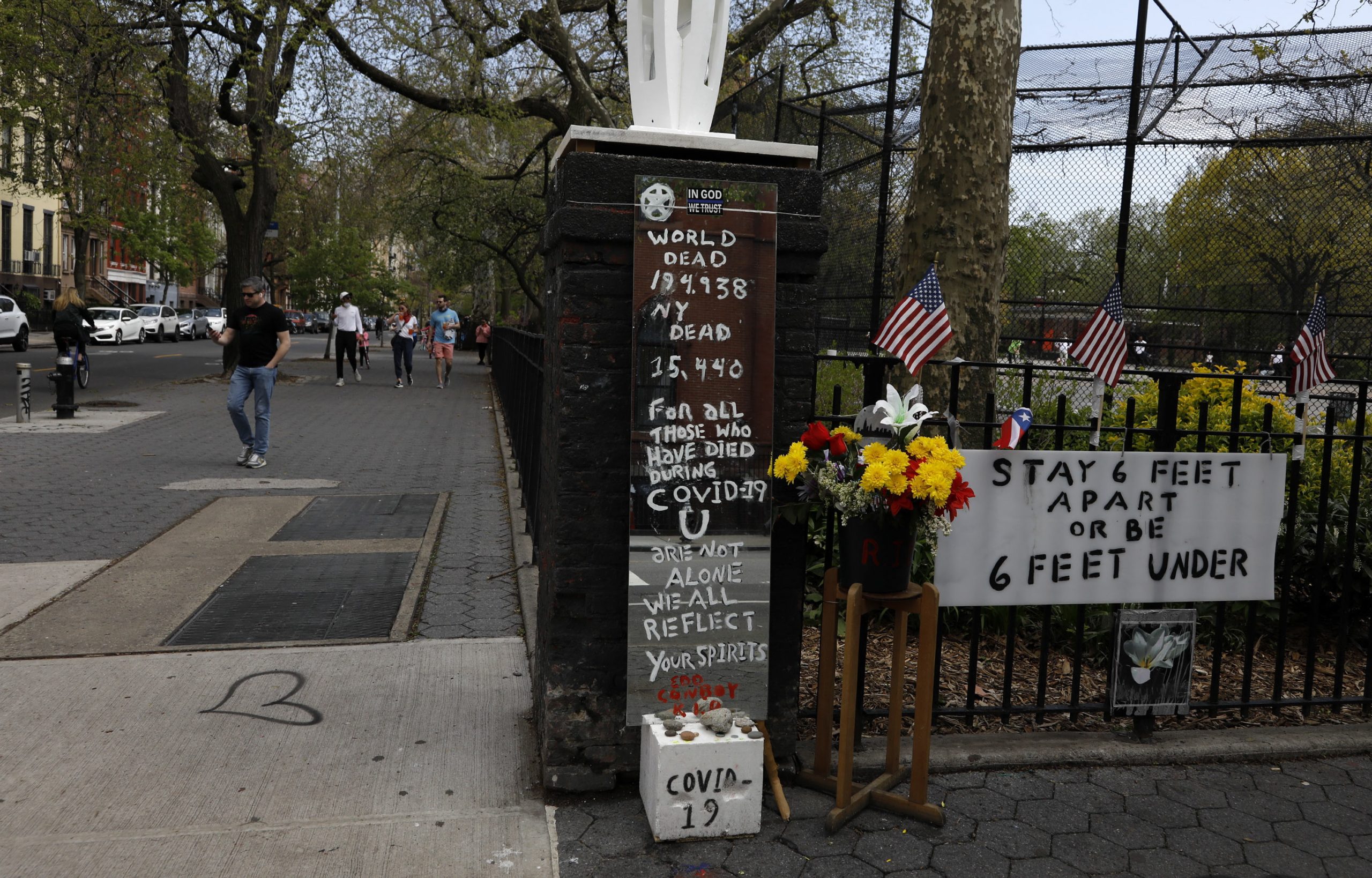 epa08384618 People without masks walk past a memorial outside of Tompkins Square Park in Alphabet City neighborhood of New York, New York, USA, 25 April 2020. Restrictions requiring the shut down of all non-essential businesses are currently in place around the United States to stop the spread of the highly-contagious coronavirus. These restrictions are having massive economic implications and some local and federal politicians are beginning to suggest plans for lifting some rules in an effort to get parts of the economy going again; many health officials are worried this will lead to another spike in COVID-19 cases.  EPA/JASON SZENES