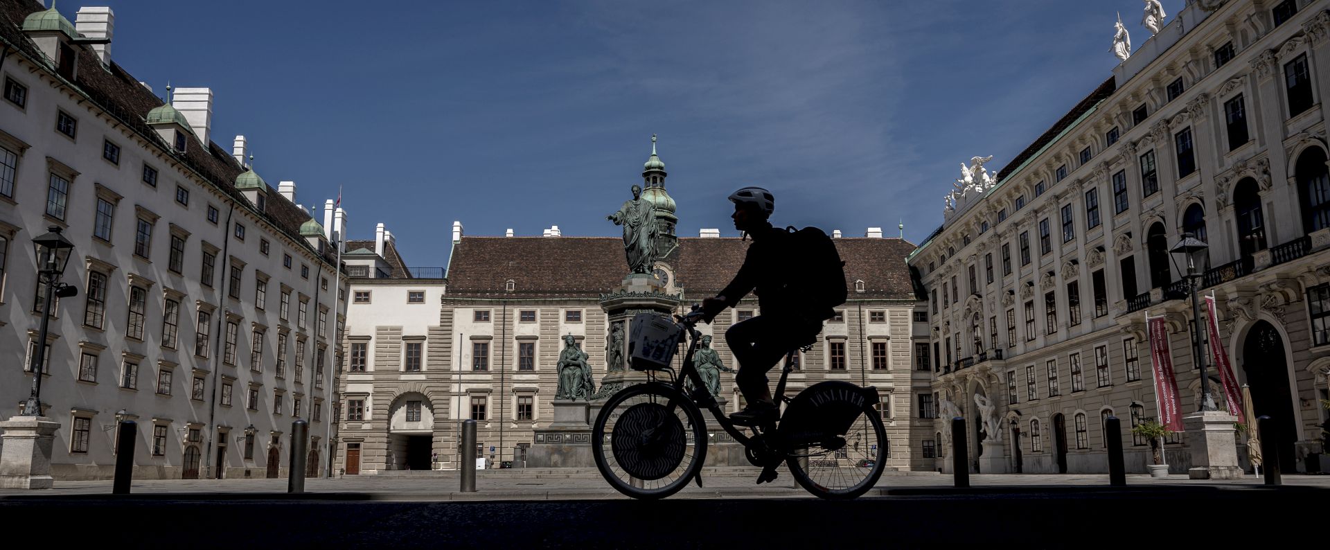 epa08366685 A cyclist rides across the Inner Castle Court (Innerer Burghof) of the Hofburg Palace in Vienna, Austria, 16 April 2020. Non essential stores with a shop area under 400 square meters, hardware stores, garden centres and federal parks are allowed to reopen under strict safety measures to slow down the ongoing pandemic of the COVID-19 disease caused by the SARS-CoV-2 coronavirus since 14 April 2020. The government has ordered to wear face masks in supermarkets, pharmacies, various kind of opened shops, public transportation and car pools.  EPA/CHRISTIAN BRUNA