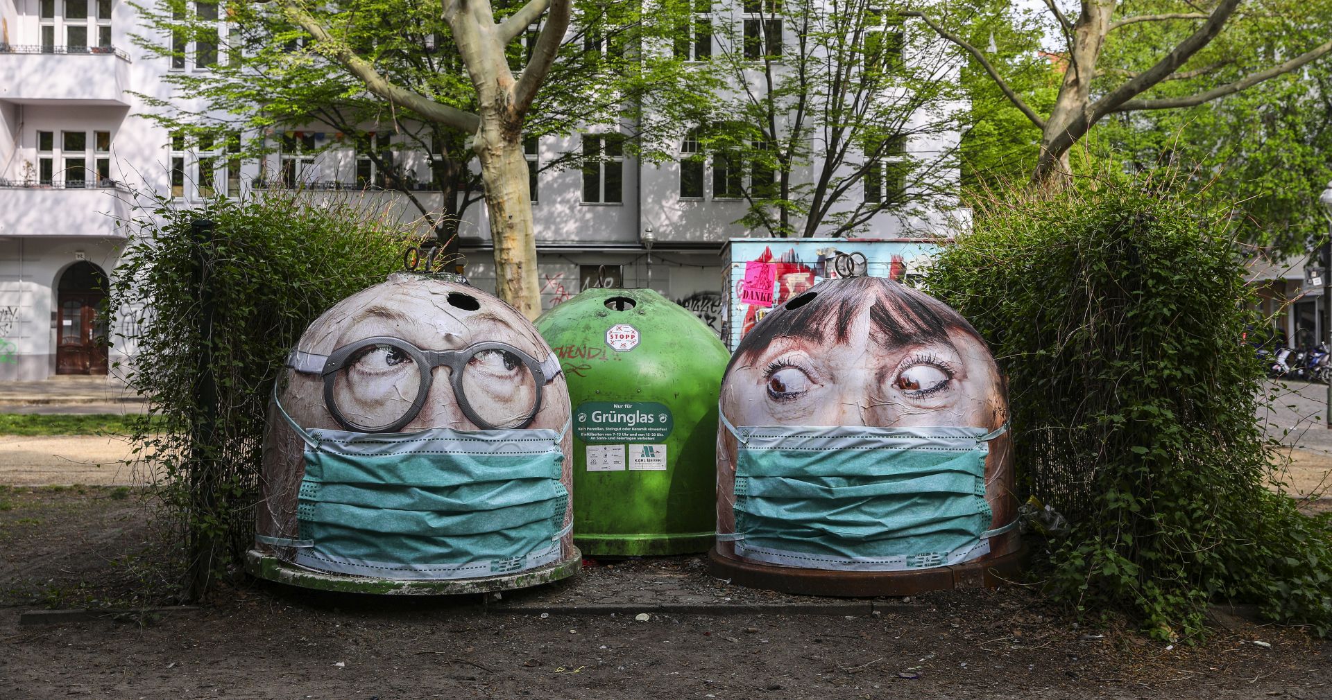 epa08392261 Glass recycle bins are covered with prints of large faces wearing surgical face masks in Berlin, Germany, 29 April 2020. The German government and local authorities are beginning to consider to gradually lift restrictions implemented to stem the spread of the coronavirus SARS-CoV-2 that causes the COVID-19 disease.  EPA/OMER MESSINGER
