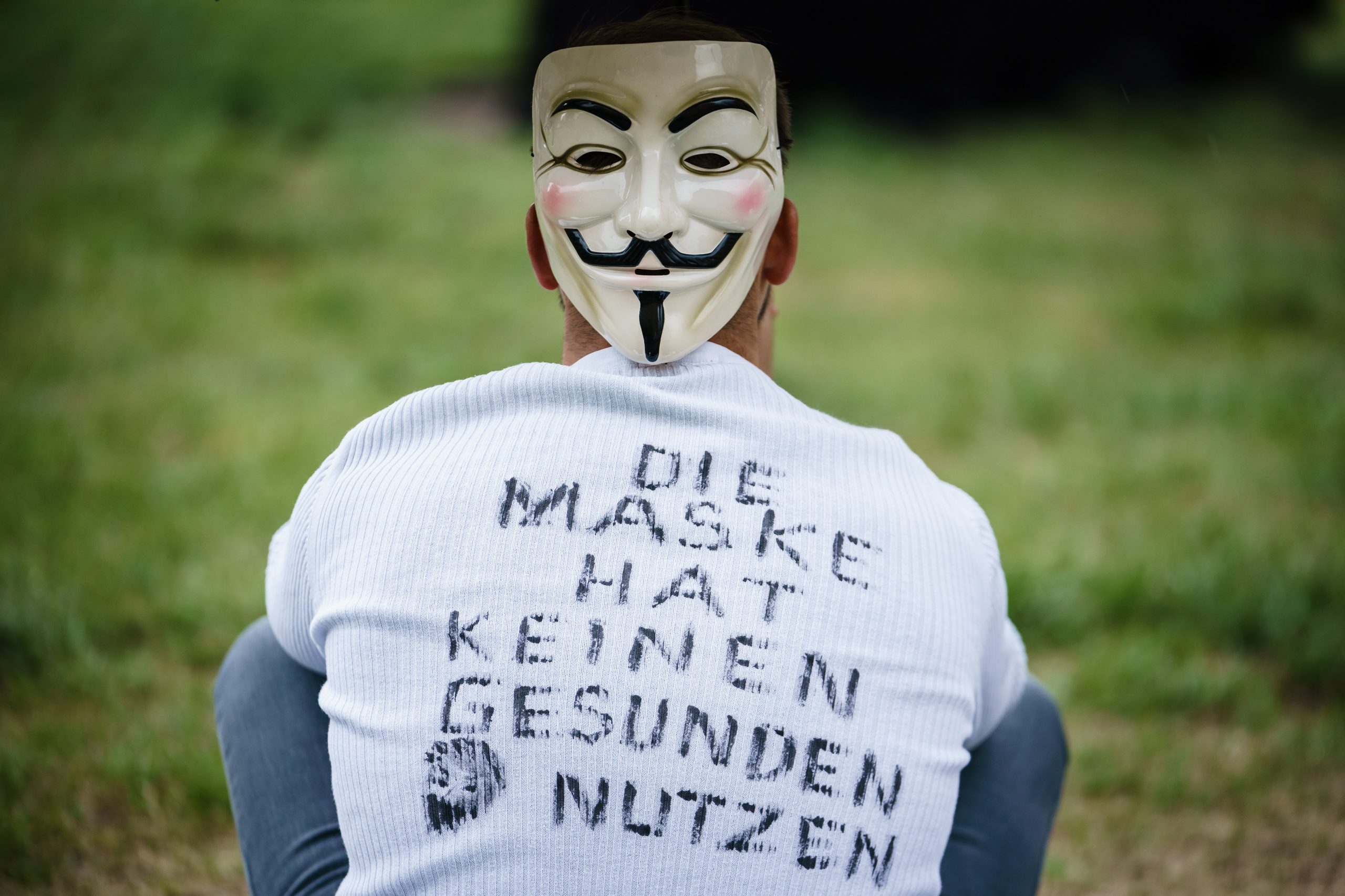 epa08397765 A protester wearing a Guy Fawkes mask and a shirt reading 'The mask has no healthy use' sits in front of the Volksbuehne theater under an umbrella during a protest in the district Mitte in Berlin, Germany, 02 May 2020. People from different political directions, like those representing the so-called 'Hygiene-Demo,' try to gather every Saturday at the Rosa-Luxemburg-Platz to protest against the restrictions and measures implemented to stem the widespread of the SARS-CoV-2 coronavirus that causes the COVID-19 disease. Counter protests take place as well, reports state. As right-wing and conspiracy theories are represented amongst some of the protesters, the Volksbuehne theater together with nearby residents express their displeasure with banners and slogans, not to be used as a scenery for right-wing protests.  EPA/CLEMENS BILAN