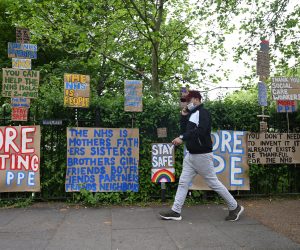 epa08398922 A masked man passes signs of support for key workers during the Covid-19 pandemic which are part of an artwork by Peter Liversidge as they are displayed on a road in east London in Britain, 03 May 2020. Countries around the world are taking increased measures to stem the widespread of the SARS-CoV-2 coronavirus which causes the Covid-19 disease.  EPA/NEIL HALL