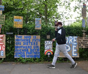 epa08398922 A masked man passes signs of support for key workers during the Covid-19 pandemic which are part of an artwork by Peter Liversidge as they are displayed on a road in east London in Britain, 03 May 2020. Countries around the world are taking increased measures to stem the widespread of the SARS-CoV-2 coronavirus which causes the Covid-19 disease.  EPA/NEIL HALL