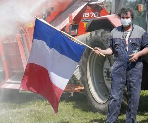 epa08407081 A farmer stands in a field holding the French flag as a tractor sprays milk powder in Lamouilly, north of France, 07 May 2020. Milk producers protest against the European Commission's way of mitigating the milk crisis.  EPA/JULIEN WARNAND