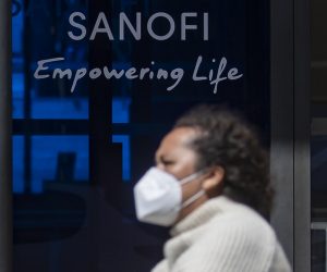 epa08424147 A woman wearing a protective face mask walks past a logo of French pharmaceutical company Sanofi in Paris, France, 15 May 2020.  The pharmaceutical giant scrapped a plan to give the United States of America priority access to a future vaccine for contributing most to the project, which sparked backlash from the French government, the company's CEO Paul Hudson later promised equal access to everyone, according to press reports.  EPA/IAN LANGSDON